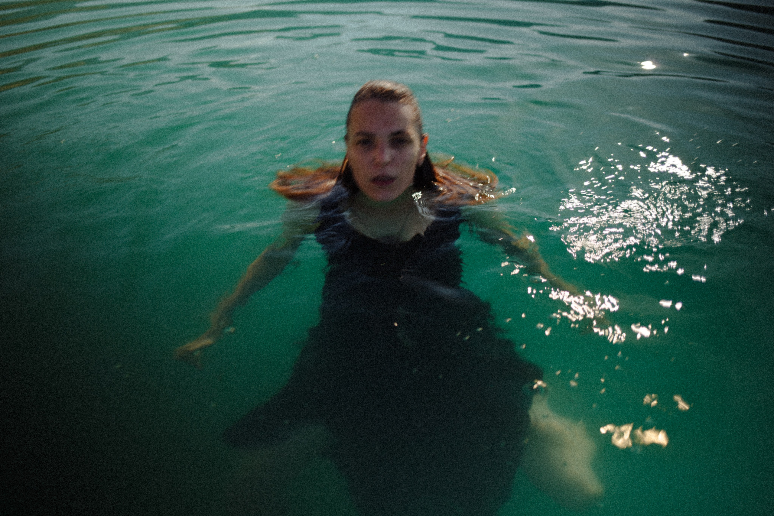 A young woman floating in a deep green body of water, smiling at the camera
