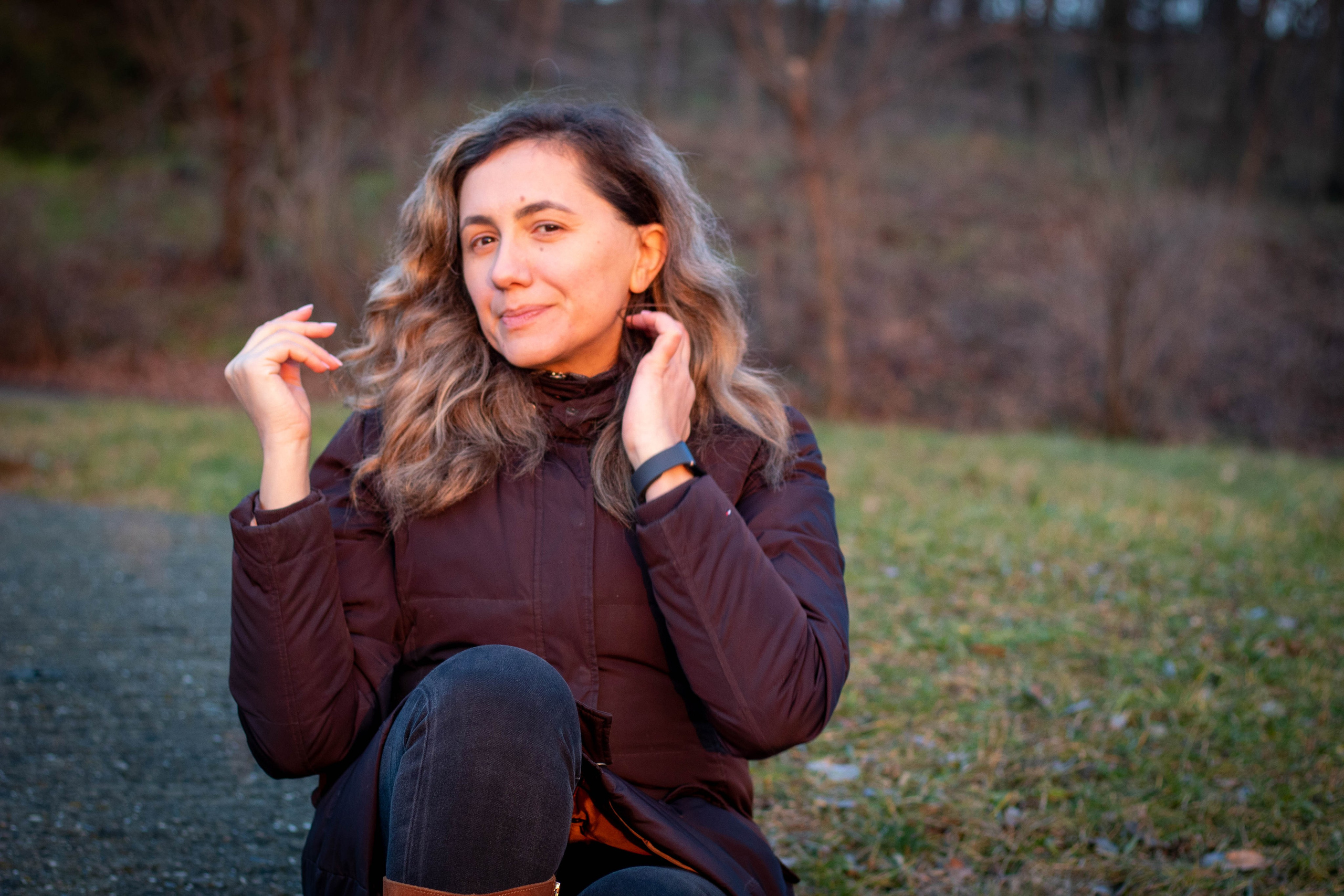 Woman sitting on the grass surrounded by fall colors, wearing a coat and gloves, with a reflective gaze.