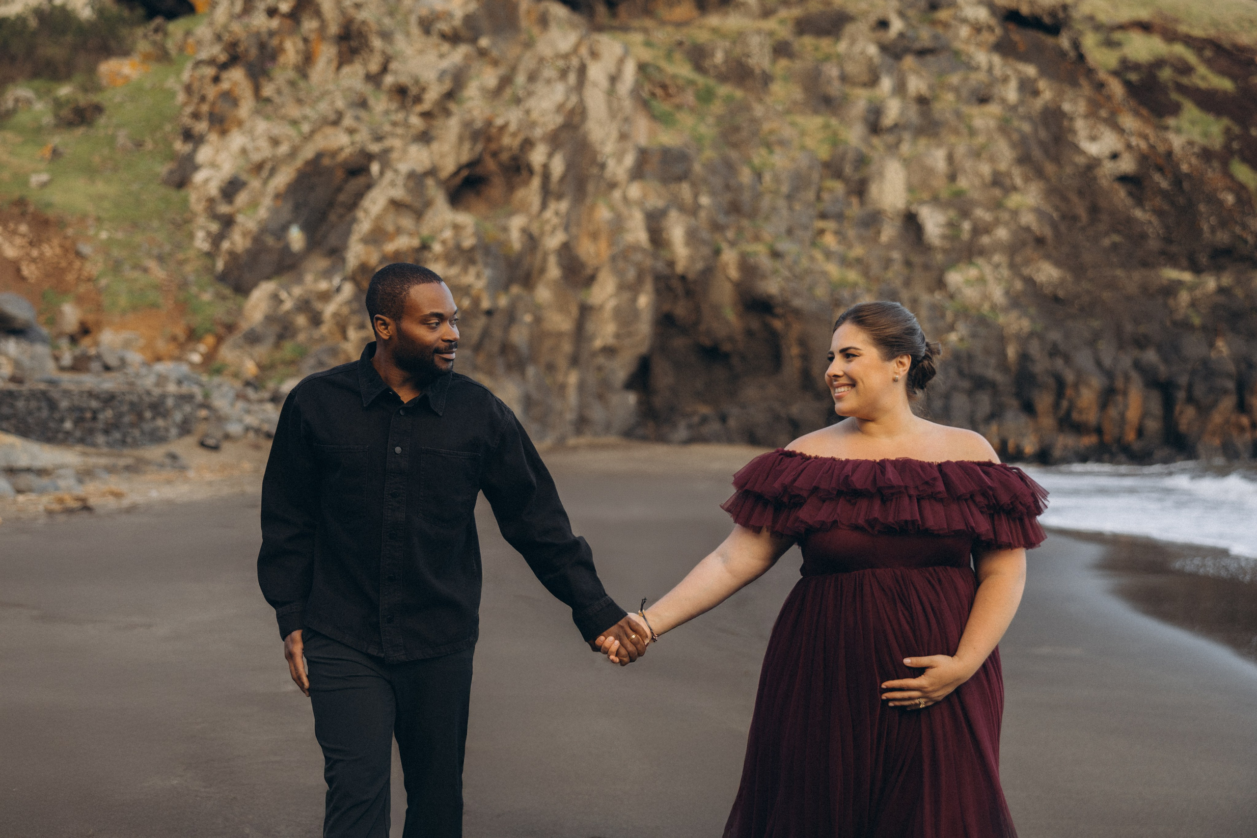 A glowing expectant mother standing on a cliff overlooking the ocean in Madeira, her dress flowing gently in the wind as the golden sunset casts a warm glow.