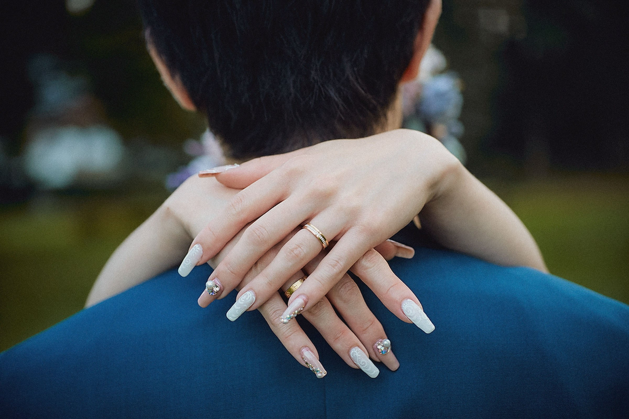 A woman's hand - showing her intricately detailed and stylish nails - rests on the back of a man's neck.