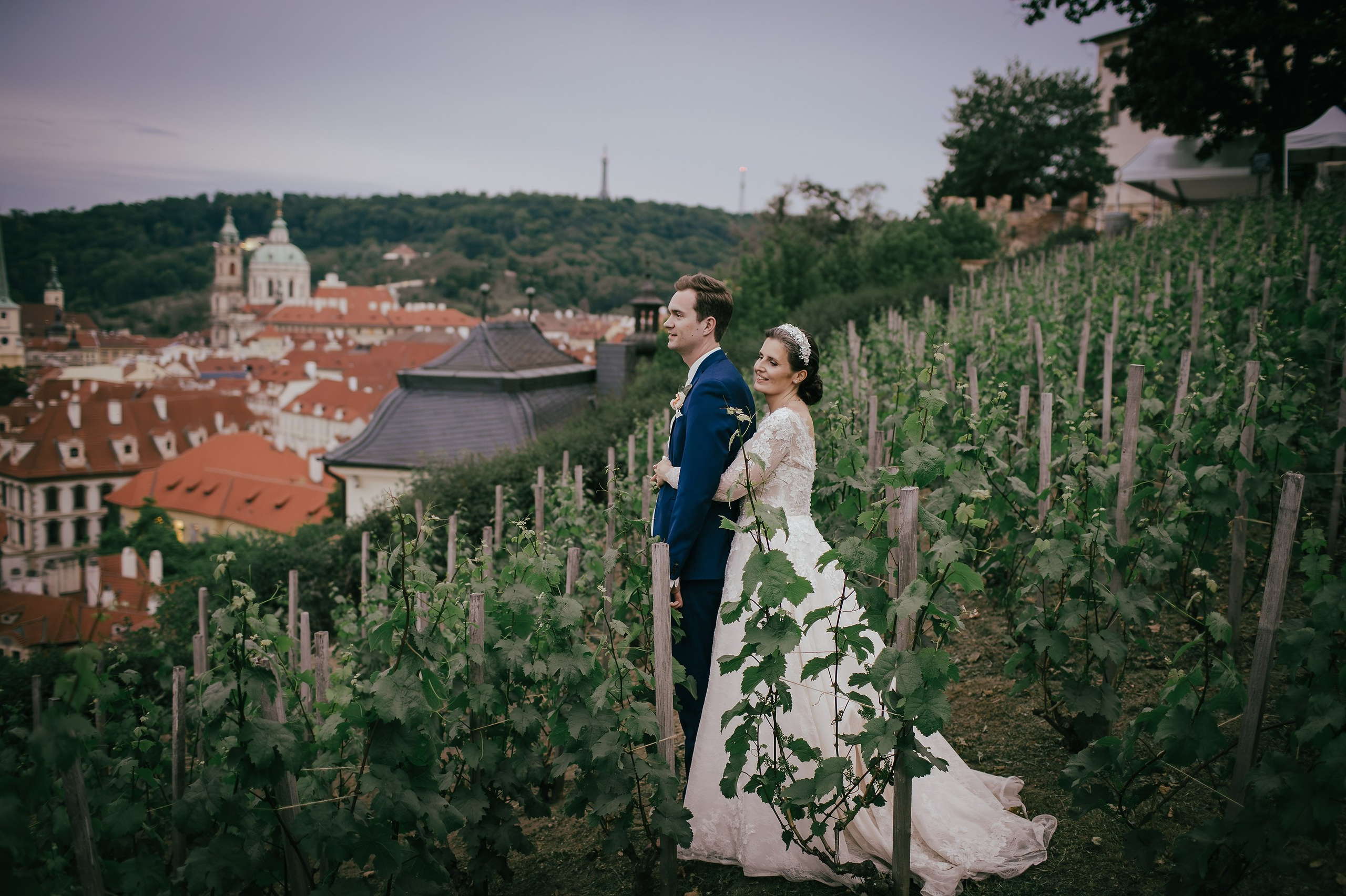 Newlyweds in a vineyard admire the twinkling city lights of Prague below them as they take a respite from wedding day celebrations at the Villa Richter.