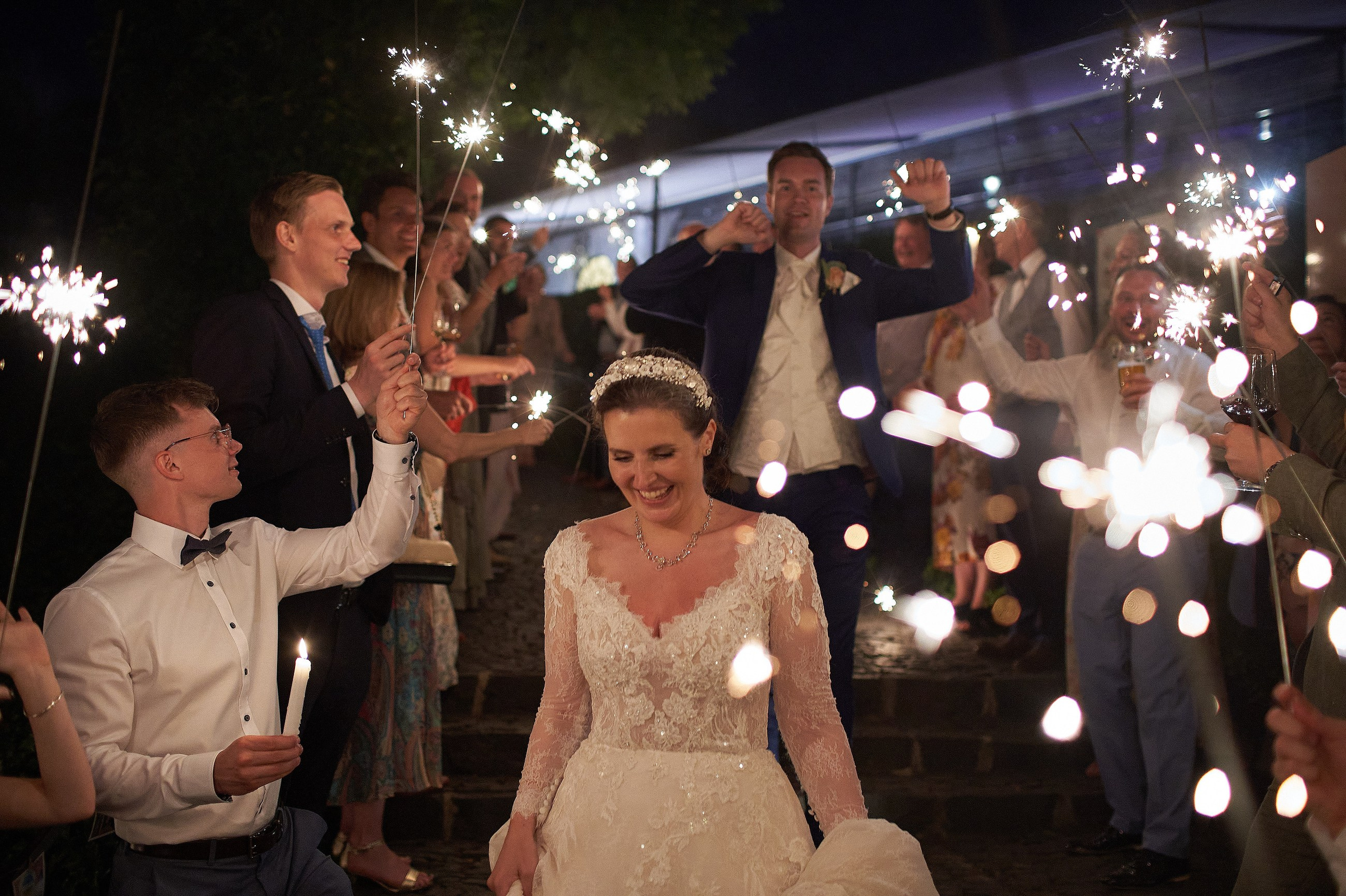 A smiling bride runs through a sparkler exit as her family & friends sing a popular song during wedding festivities at the Villa Richter in Prague.
