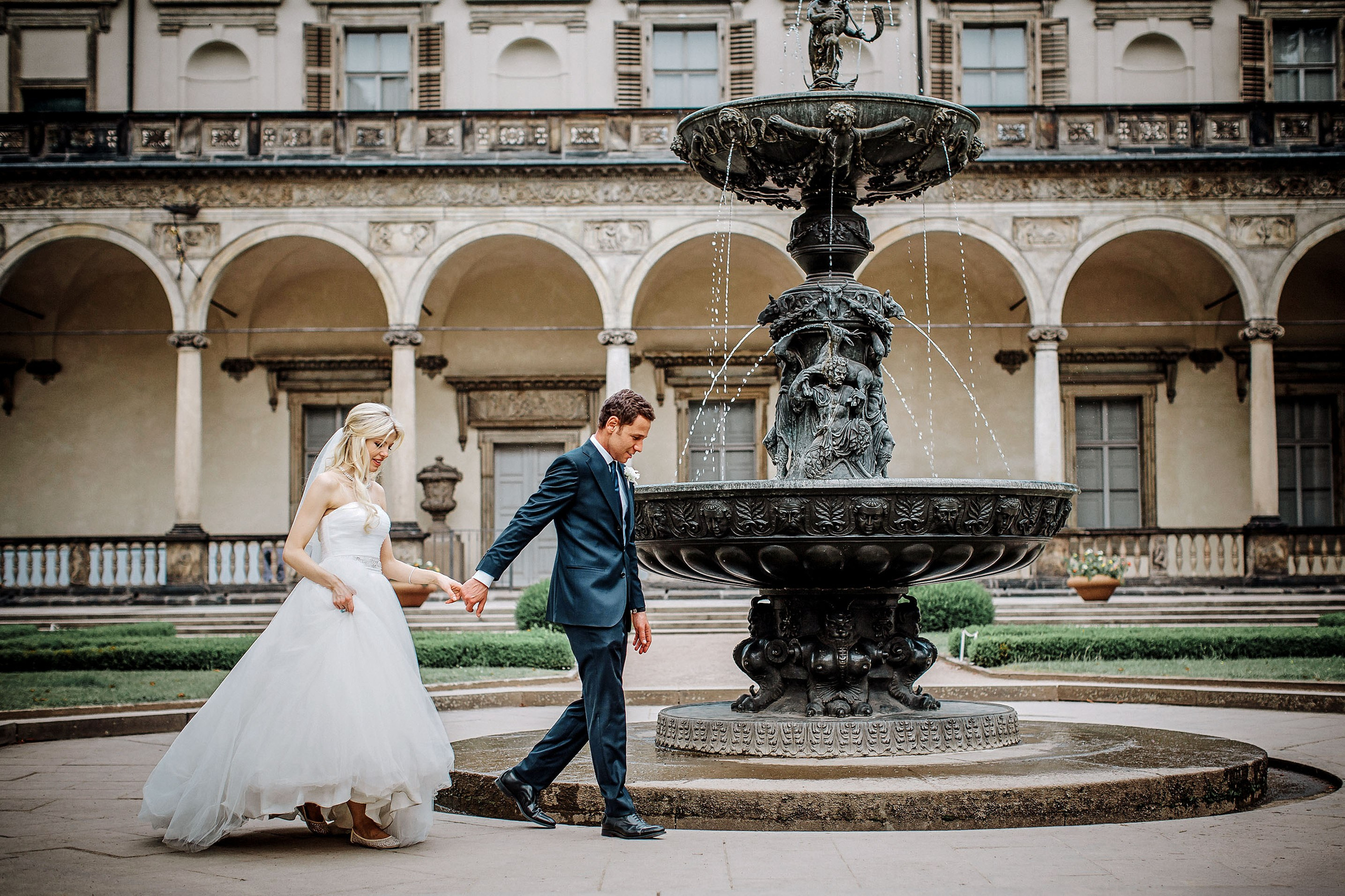 Blonde bride and Italian groom by Queen Anne's Fountain, Prague Castle grounds.