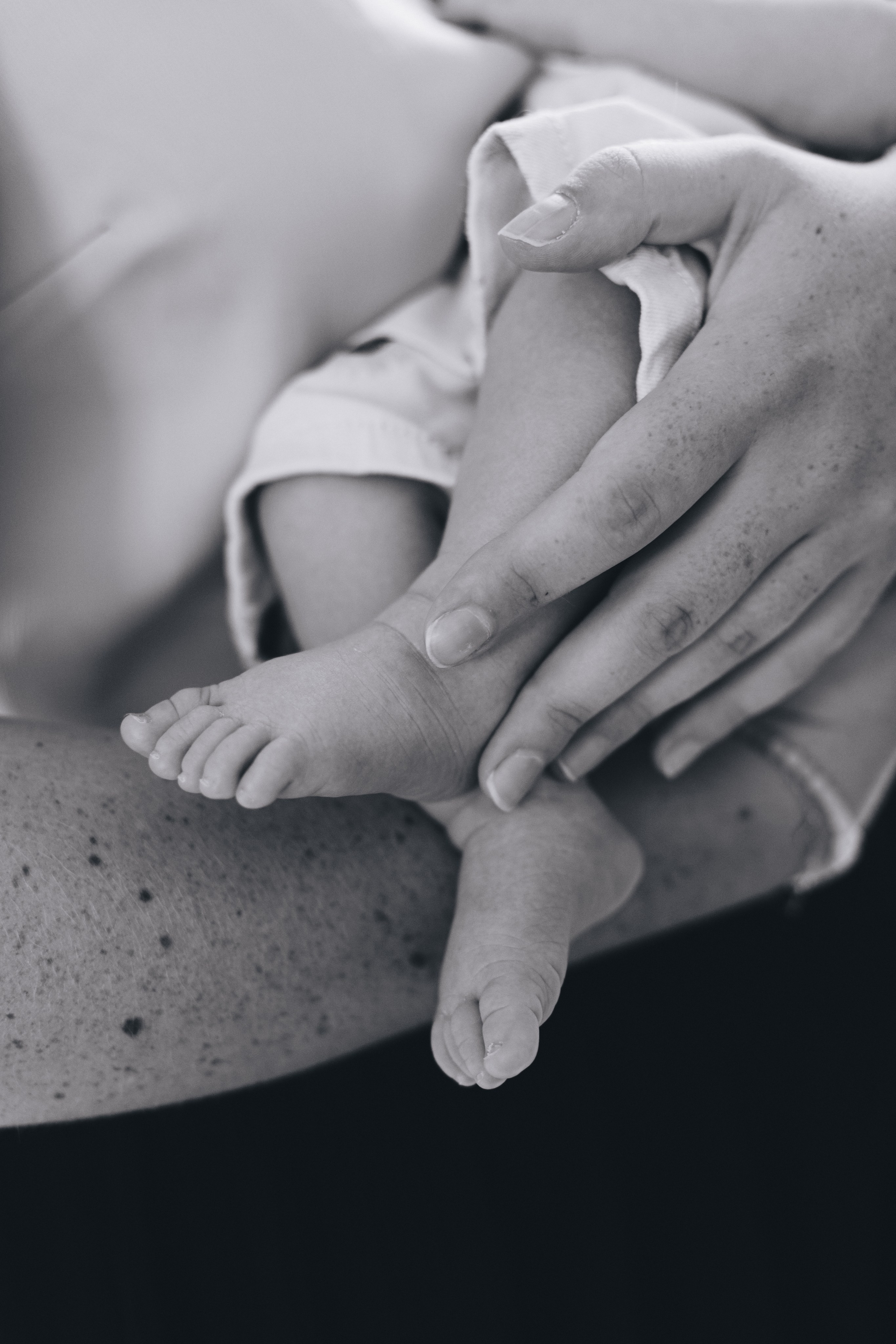 Mamas Hand umarmt die kleinen Füße des Babys.