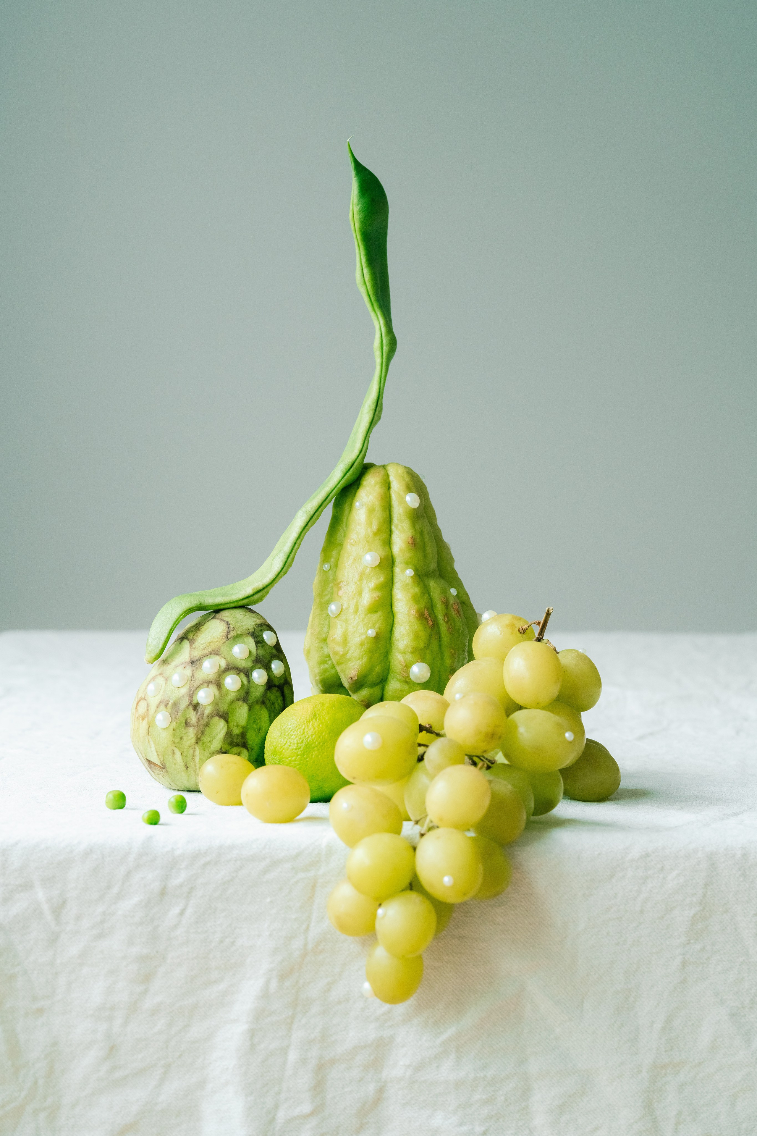Still Life criativo com produtos verdes e contas brancas. Um arranjo artístico de produtos verdes, incluindo uvas, chayote e ervilhas, adornado com contas brancas.