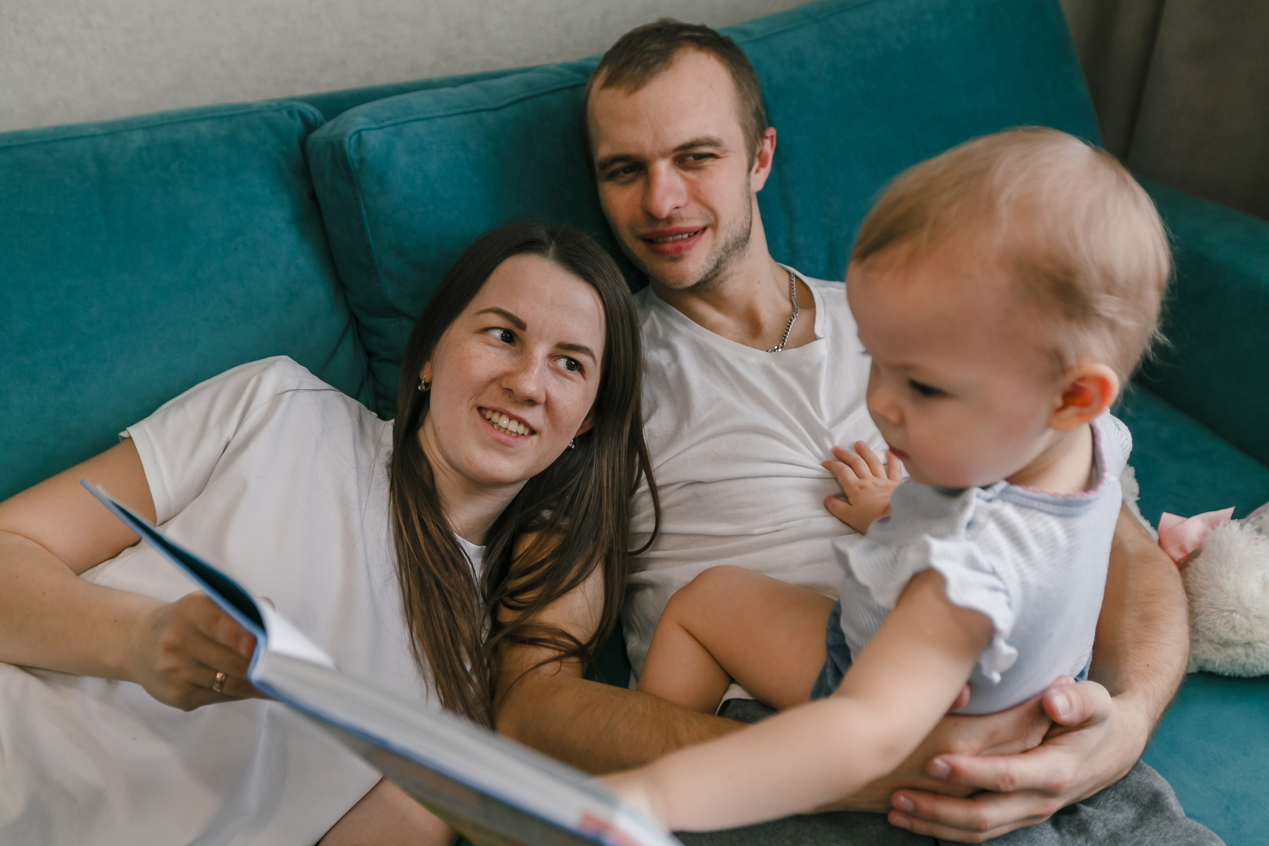 padres leyendo un libro a su hija mientras están acostados en el sofá