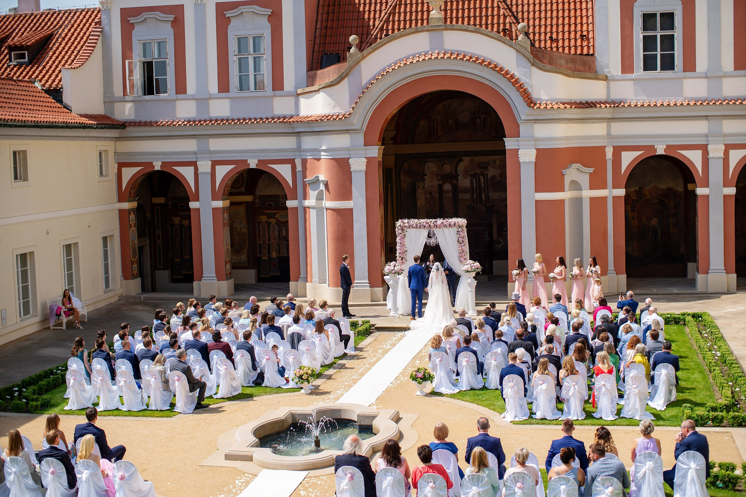 A wide angle view from above shows the historic Ledebour garden with its storied architecture and painted walls as wedding guests watch the wedding ceremony.
