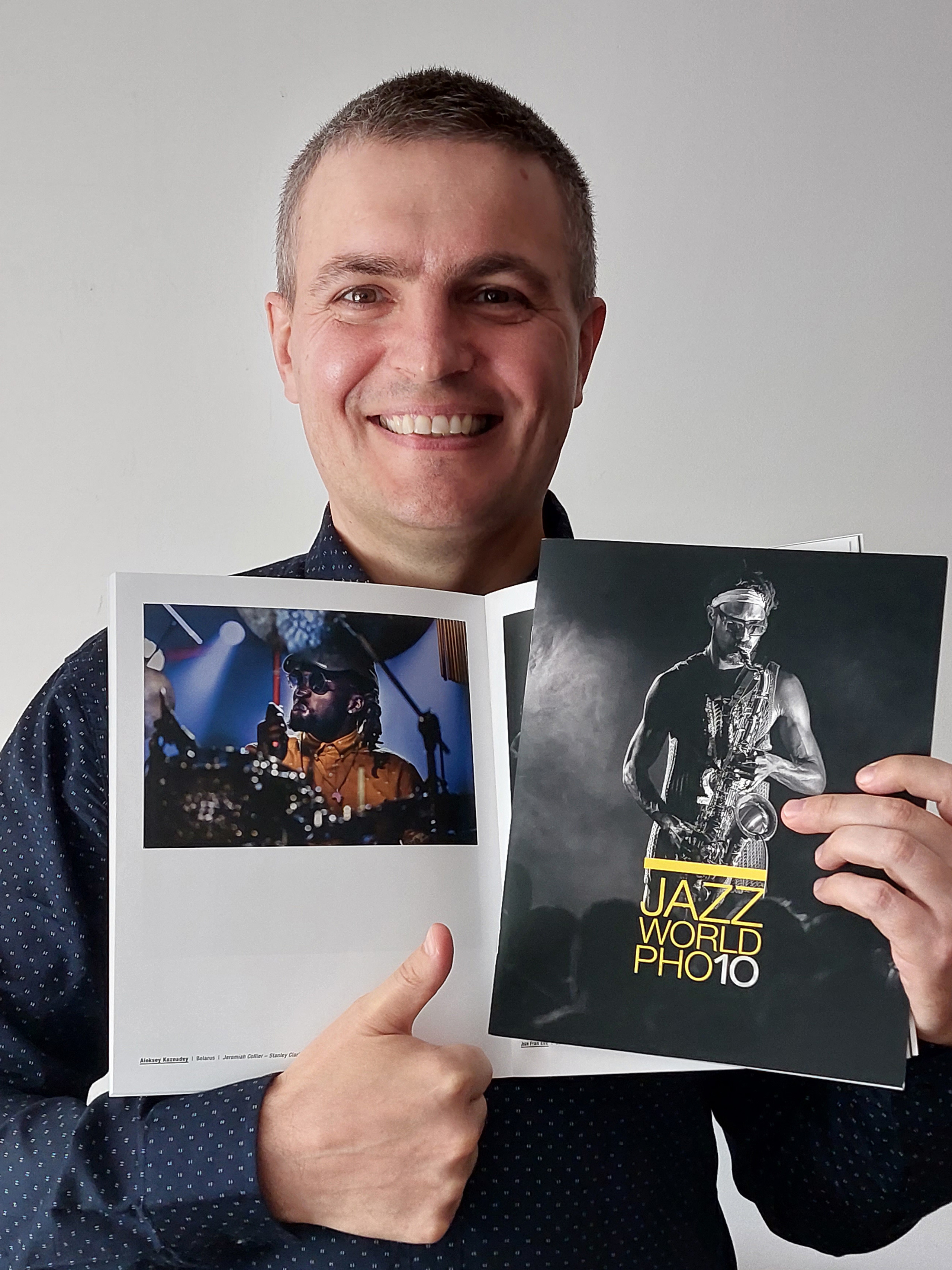 Szczęśliwy Aleksiej Kaznadziej ze stroną ze swoim zdjęciem i okładką katalogu Jazz World Photo'2023.