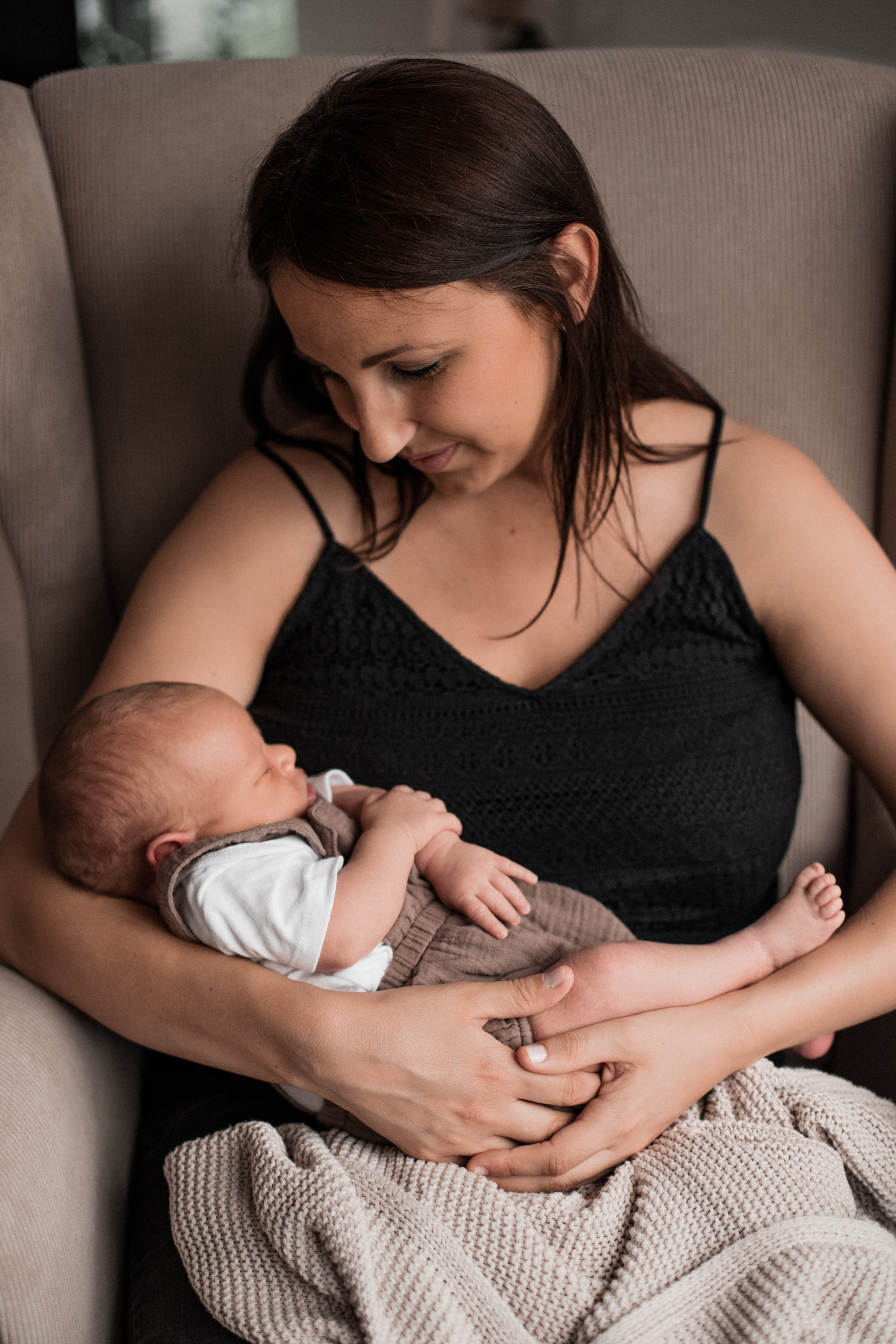 Mutter sitzt im Sessel und hält ihren kleinen Sohn im Arm.