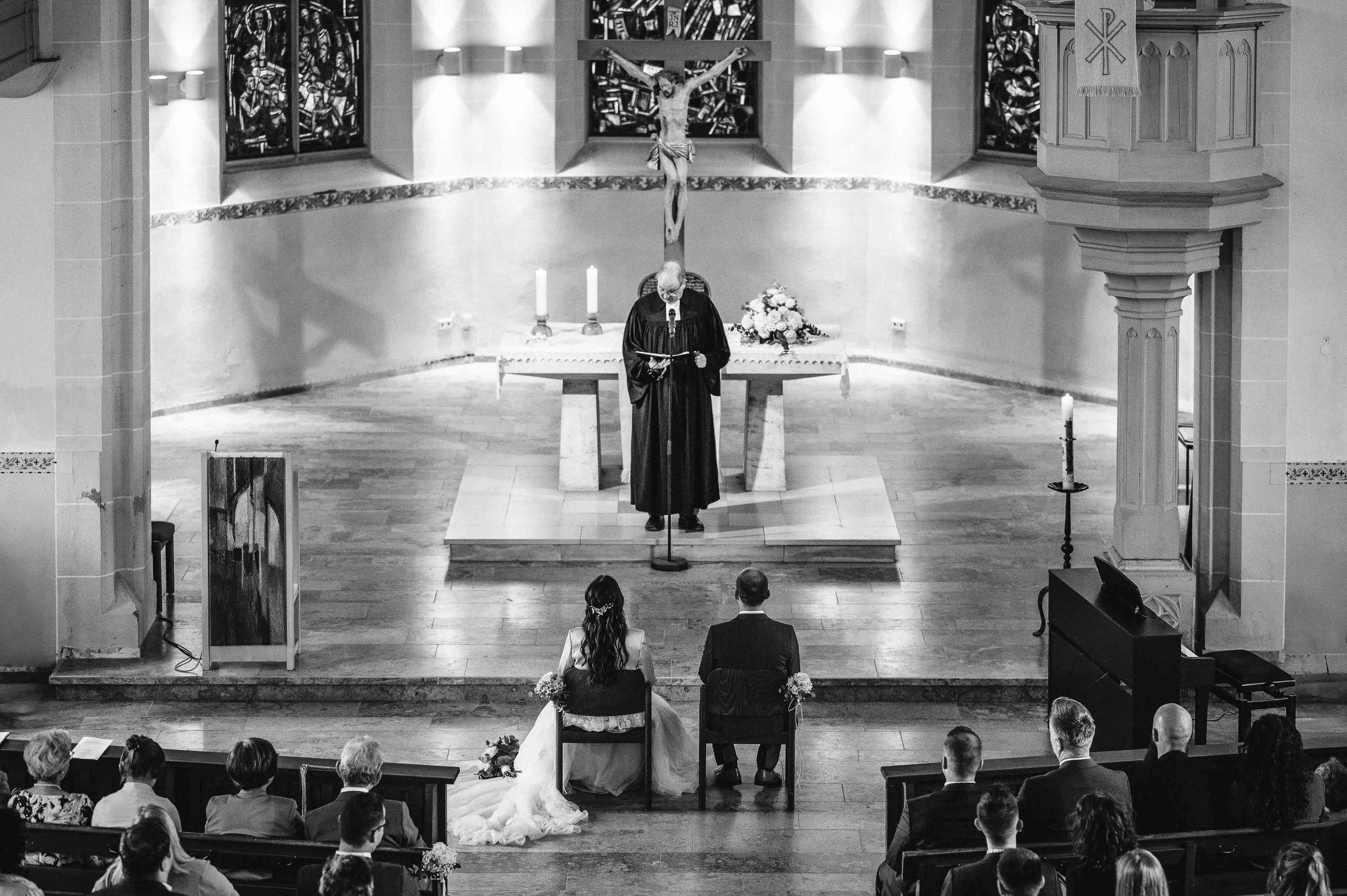 Brautpaar sitzt in der Kirche, beobachtet Predigt des Pfarrers.