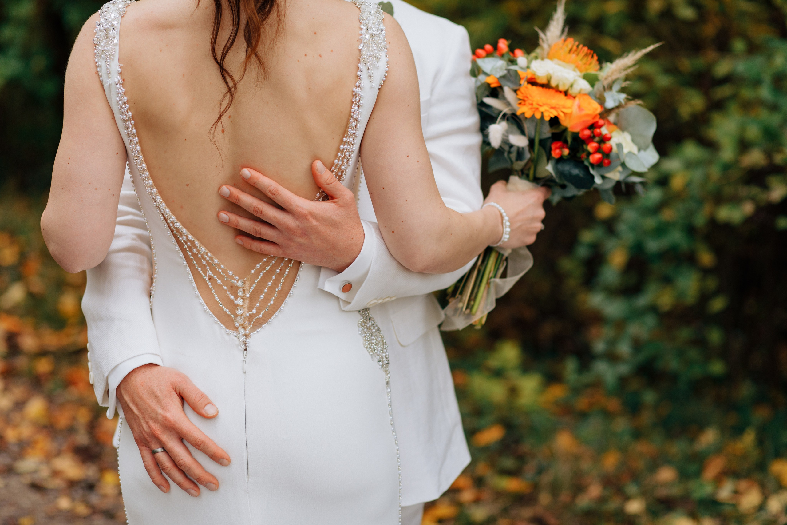 Die Hand des Bräutigams liegt auf der schönen, offenen Rücken der Braut, während die andere auf ihrer Hüfte ruht.