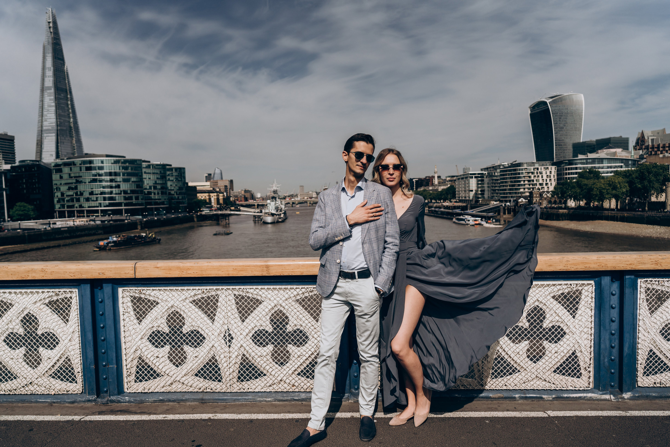 young couple standing on the top of the bridge, wind is blowing dress 