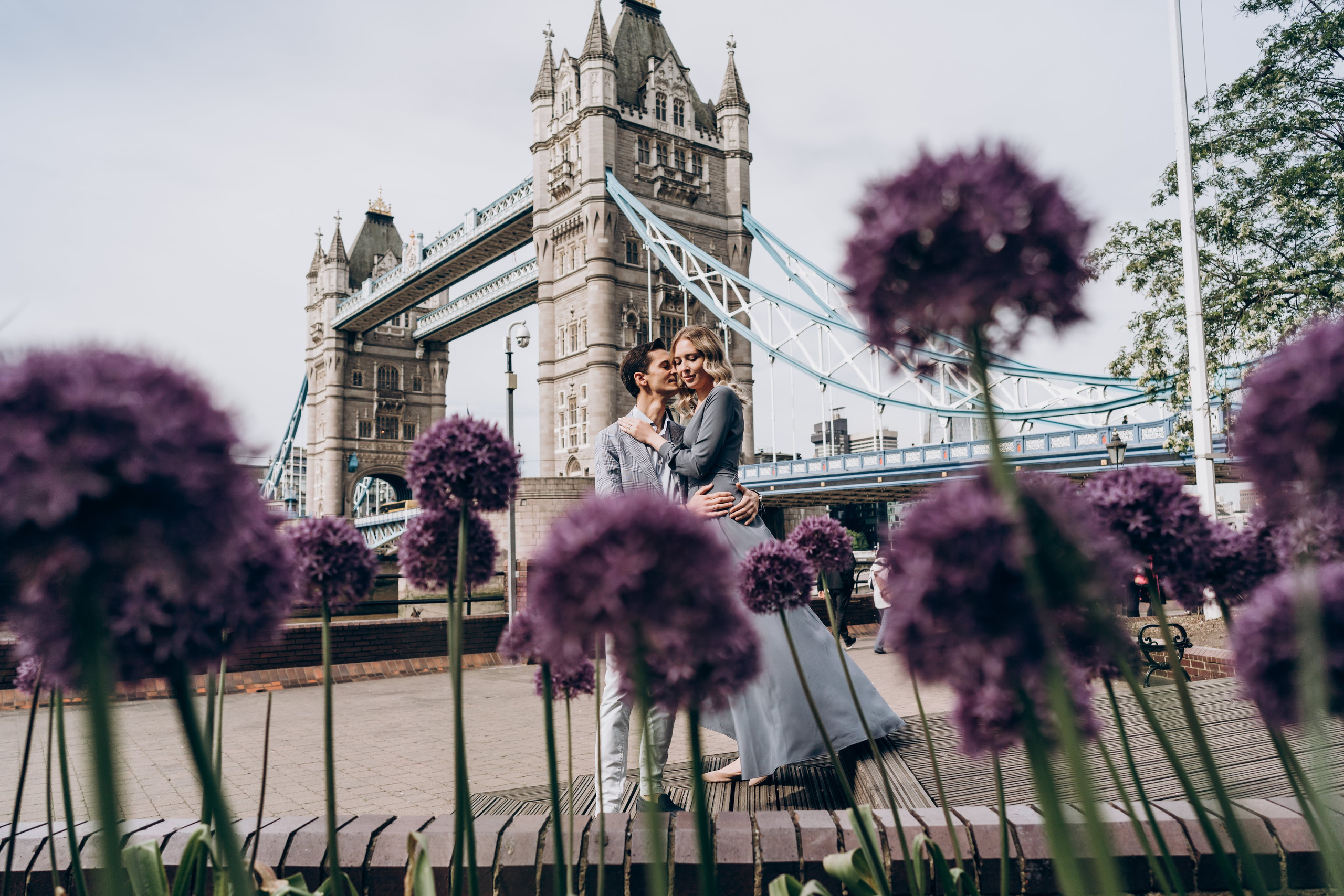 young couple posing with purple flowers by tower bridge 