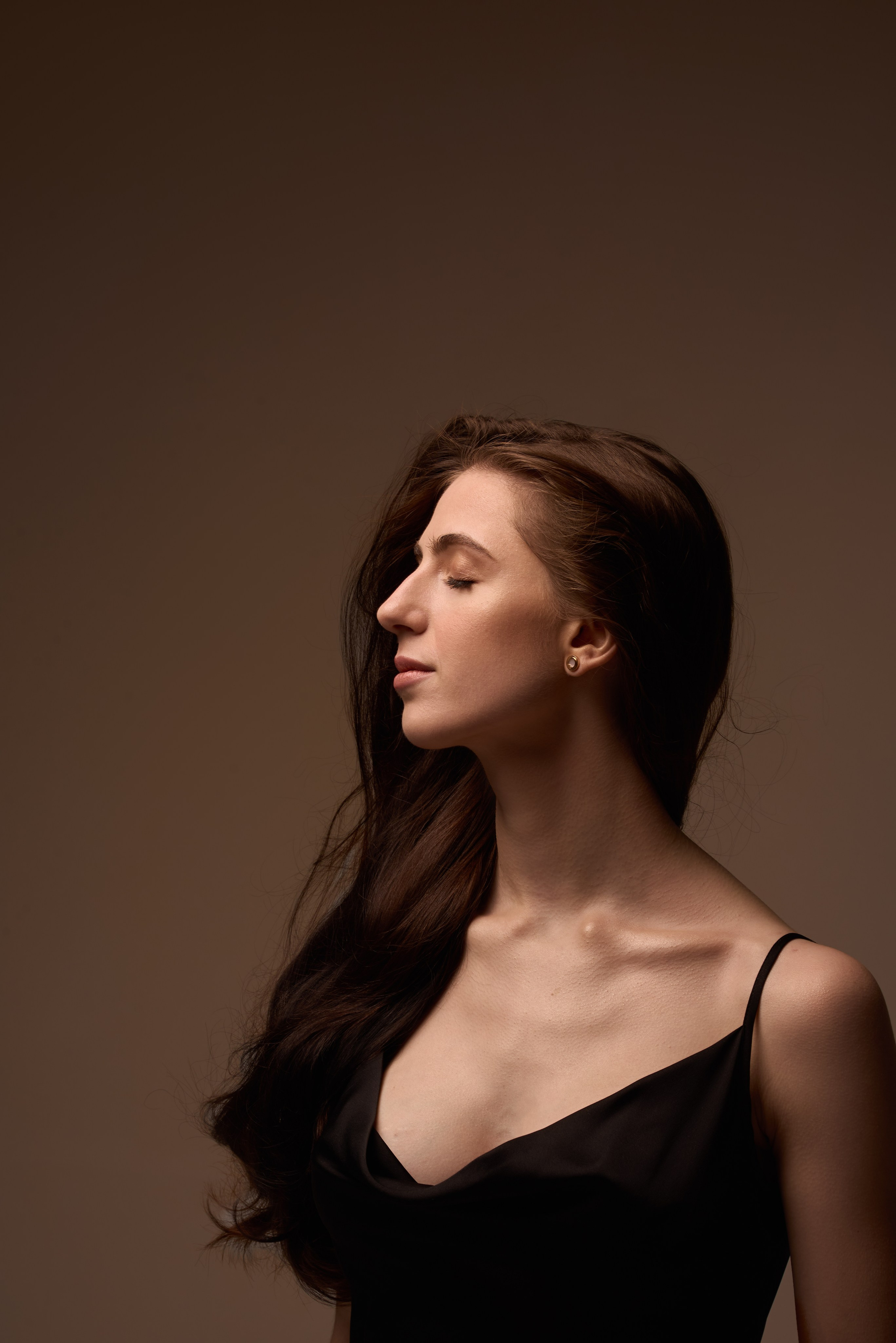 Artystyczna sesja portretowa – kobieta w czarnej sukience na brązowym tle, naturalne piękno i delikatność.