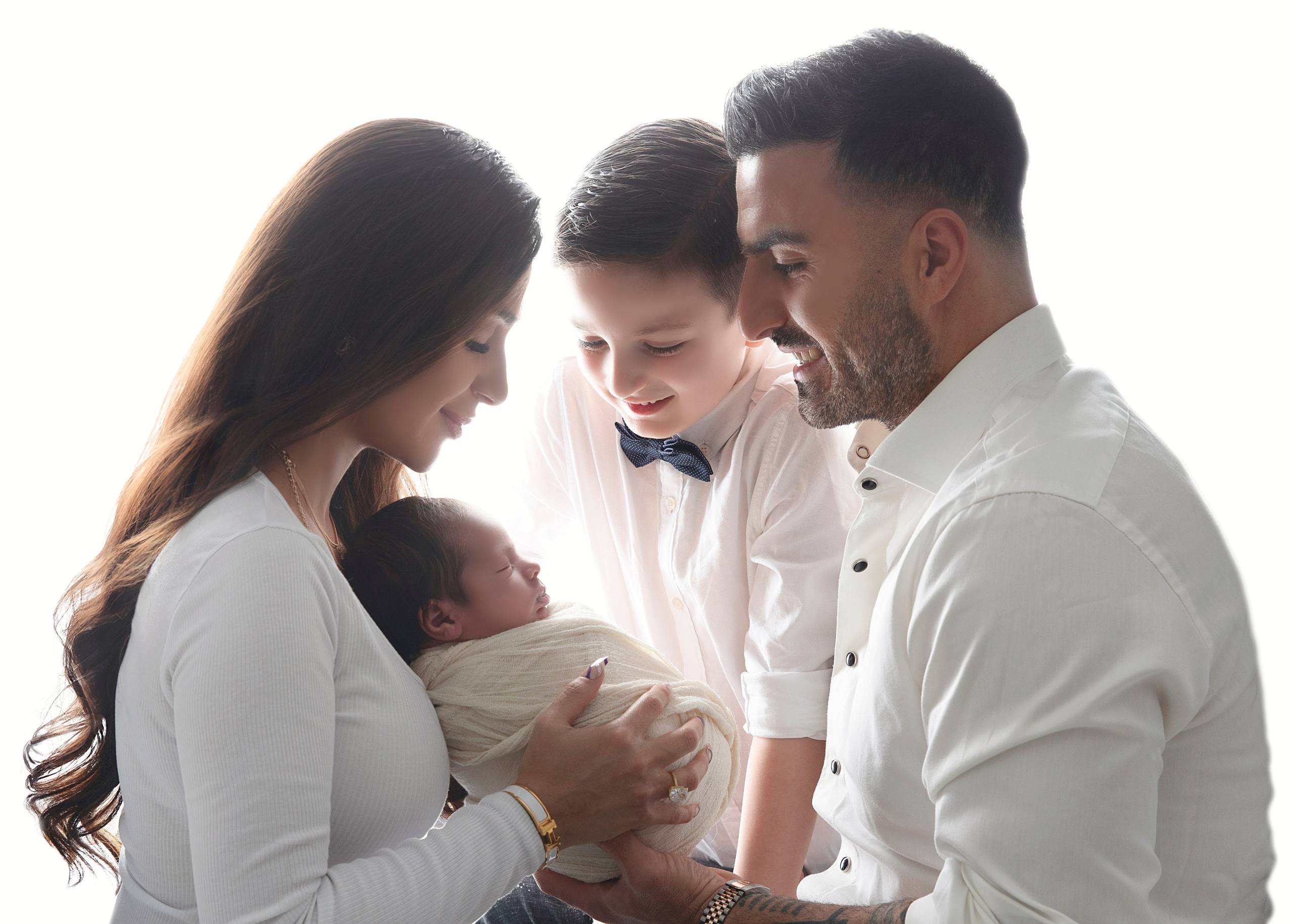 "Familjebild där föräldrarna sitter med sina nyfödda barn och äldre syskon. Bilden visar den ömma och kärleksfulla relationen mellan familjemedlemmarna och den nya tillskottet till familjen."