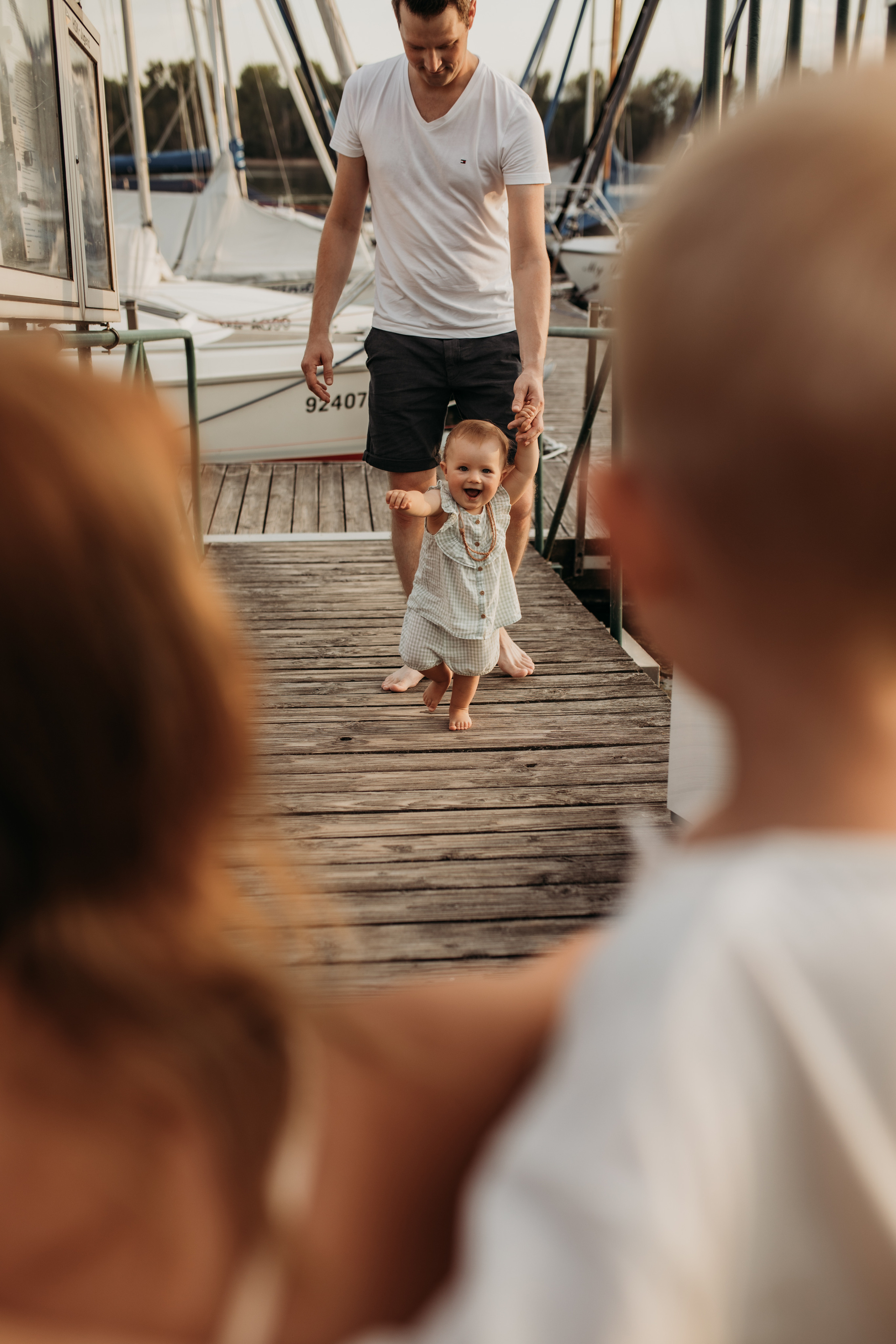 Kleines Mädchen hält Hand von Papa und rennt zu Mamaauf dem Strand beim Familienshooting in der Nähe von Speyer.