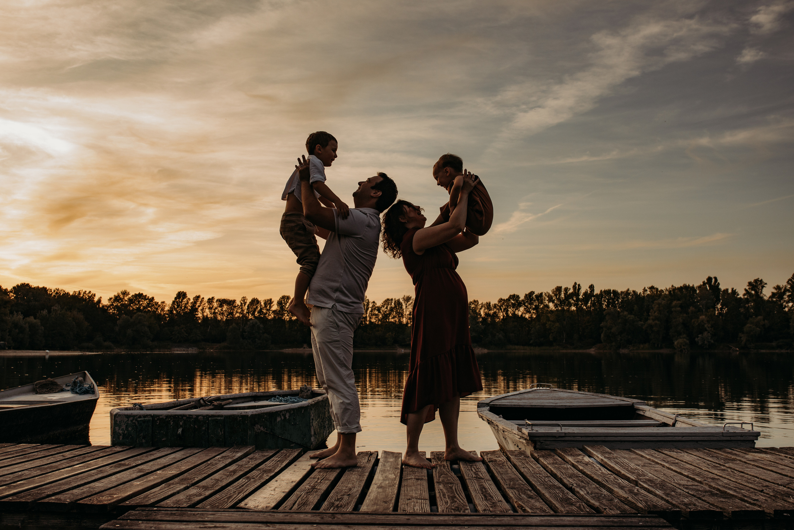Eltern halten ihre zwei Kinder hoch beim Sonnenuntergang am See beim Kindershooting.