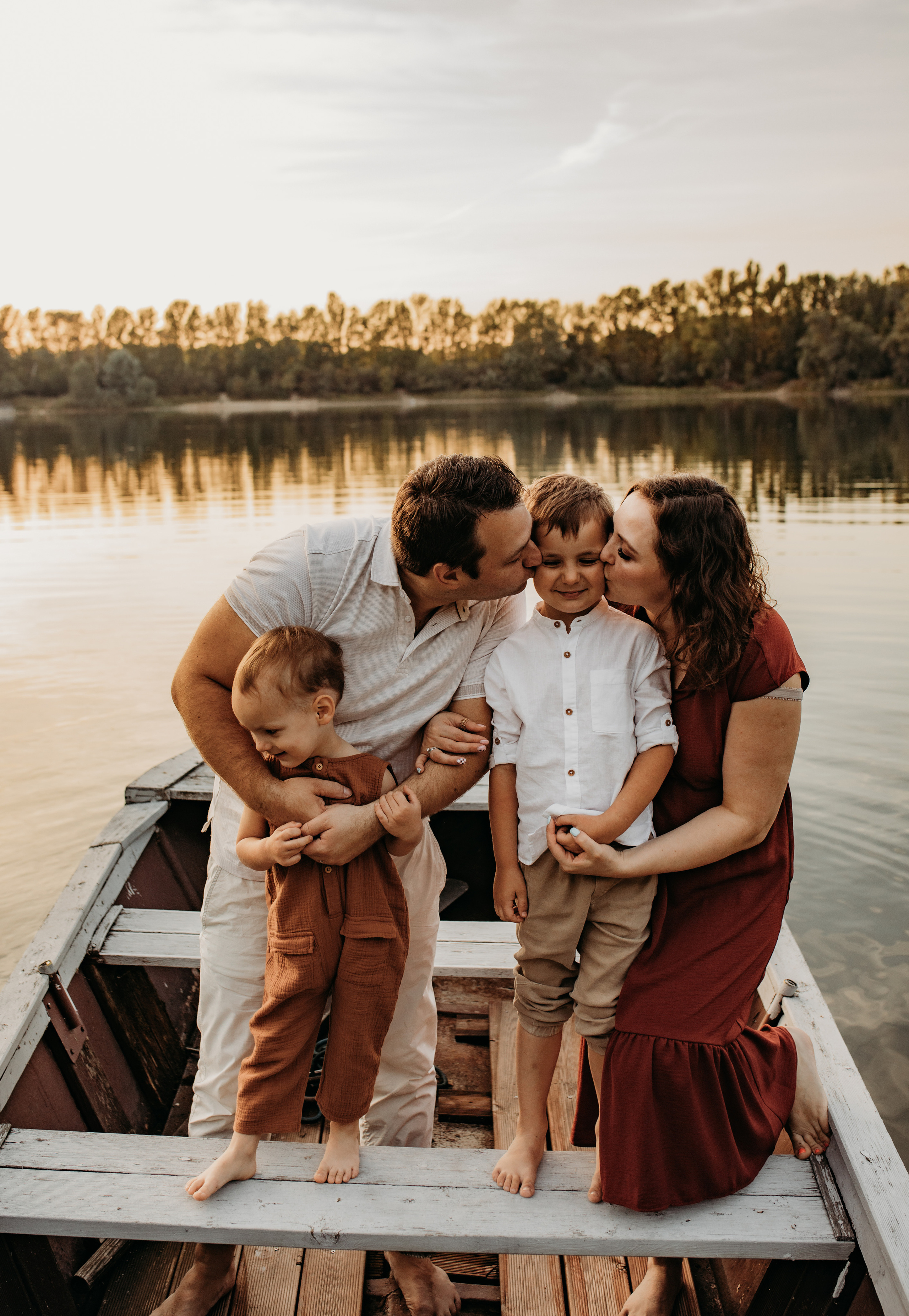 Eltern küssen ihren Sohn stehend im Boot beim Sonnenuntergang beim Fotoshooting in Heidelberg.