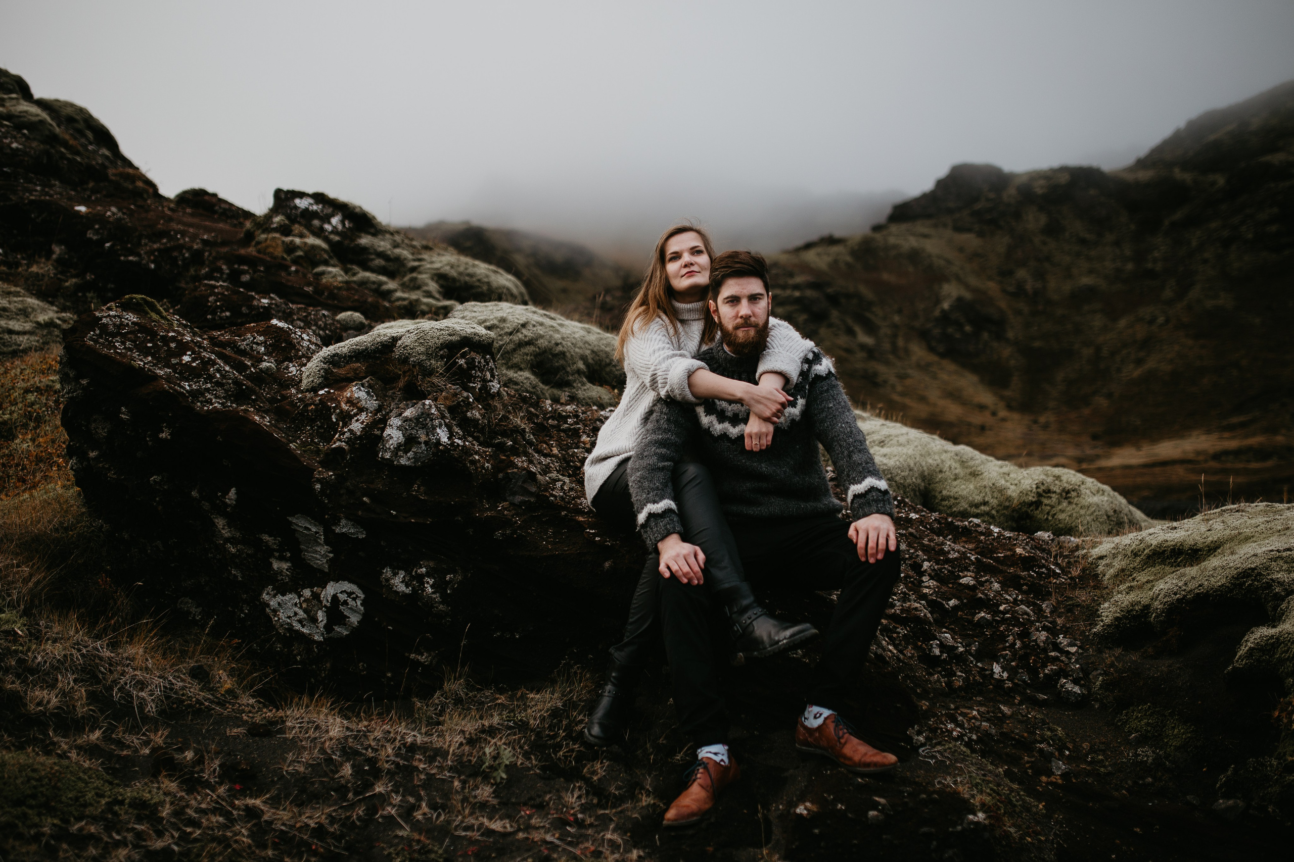 Adventurous couple standing on a black sand beach in Iceland, with dramatic cliffs in the background.  Reykjanes Peninsula