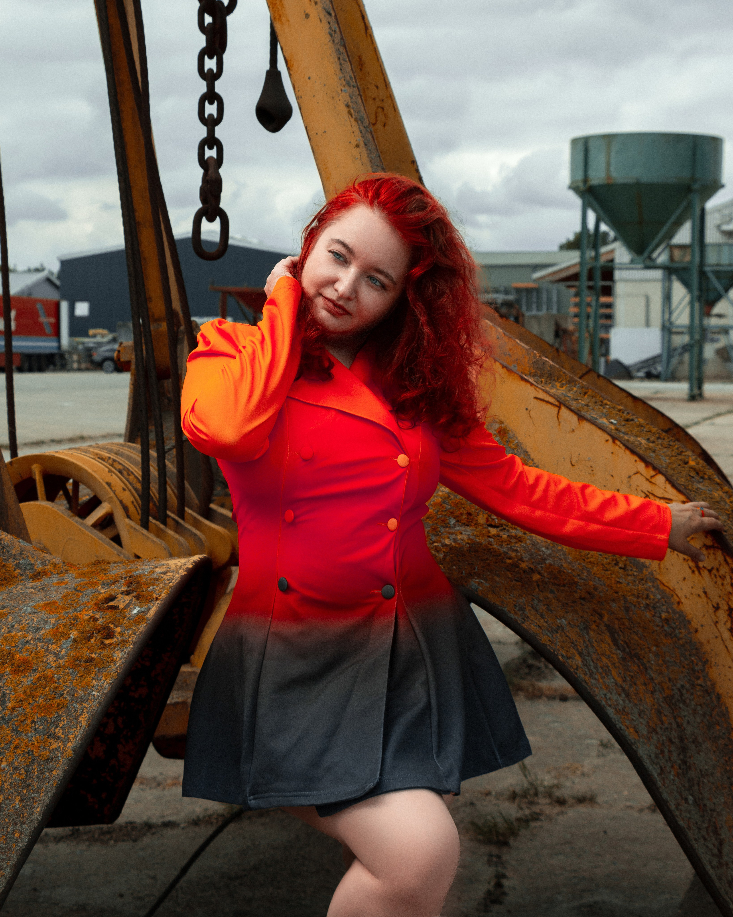 Outdoor-Porträt einer Frau mit feuerroten Haaren und rotem Kleid vor Fabrik