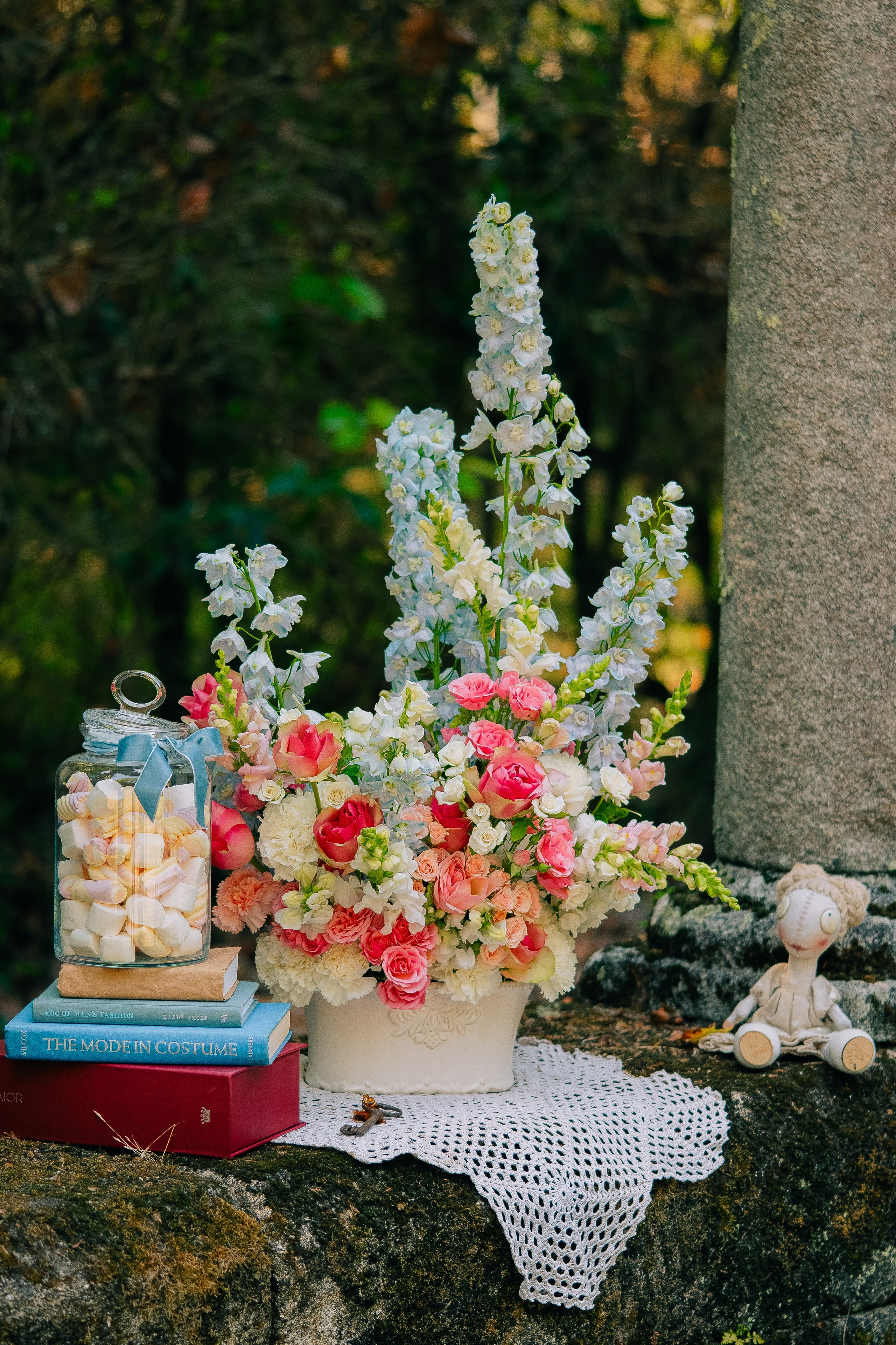 Arranjo floral com livros e decoração vintage. Bela peça central floral com flores cor-de-rosa e branco, livros e um frasco de vidro de doces, dispostos em uma superfície rústica.