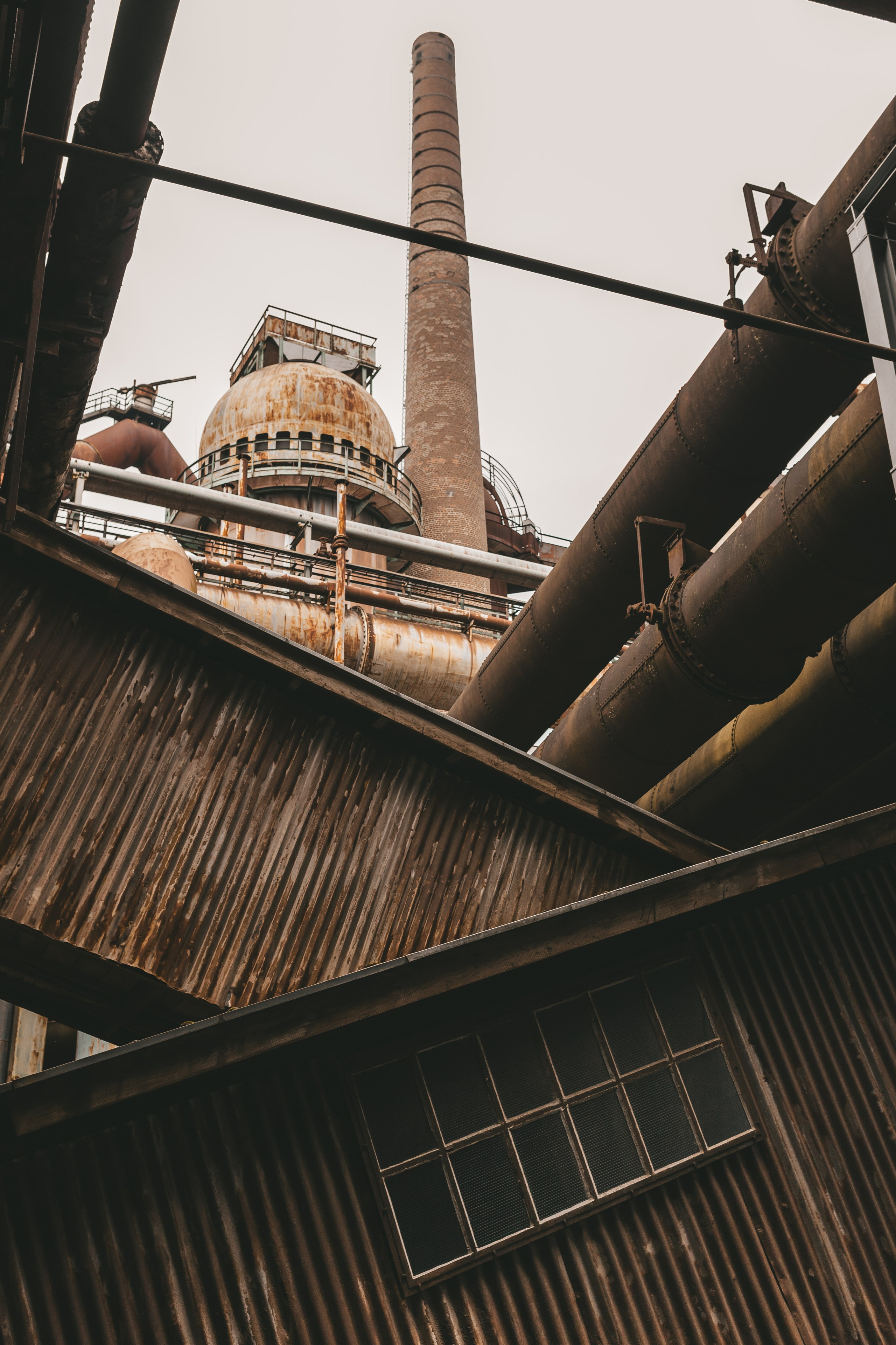 Силуэт доменной печи и труб на фоне светлого неба.