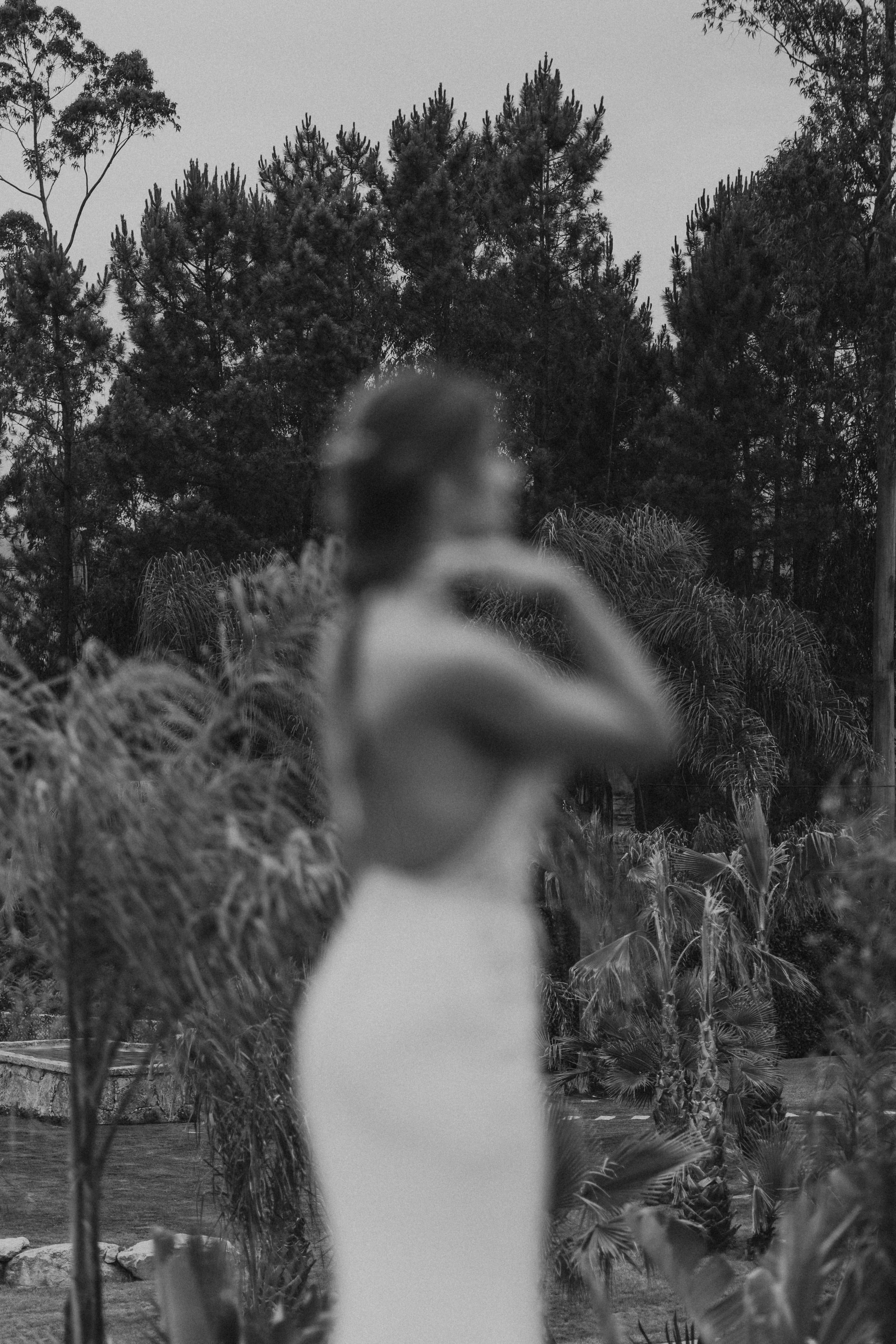 Noiva caminha por jardim arborizado em momento sereno antes da cerimónia.