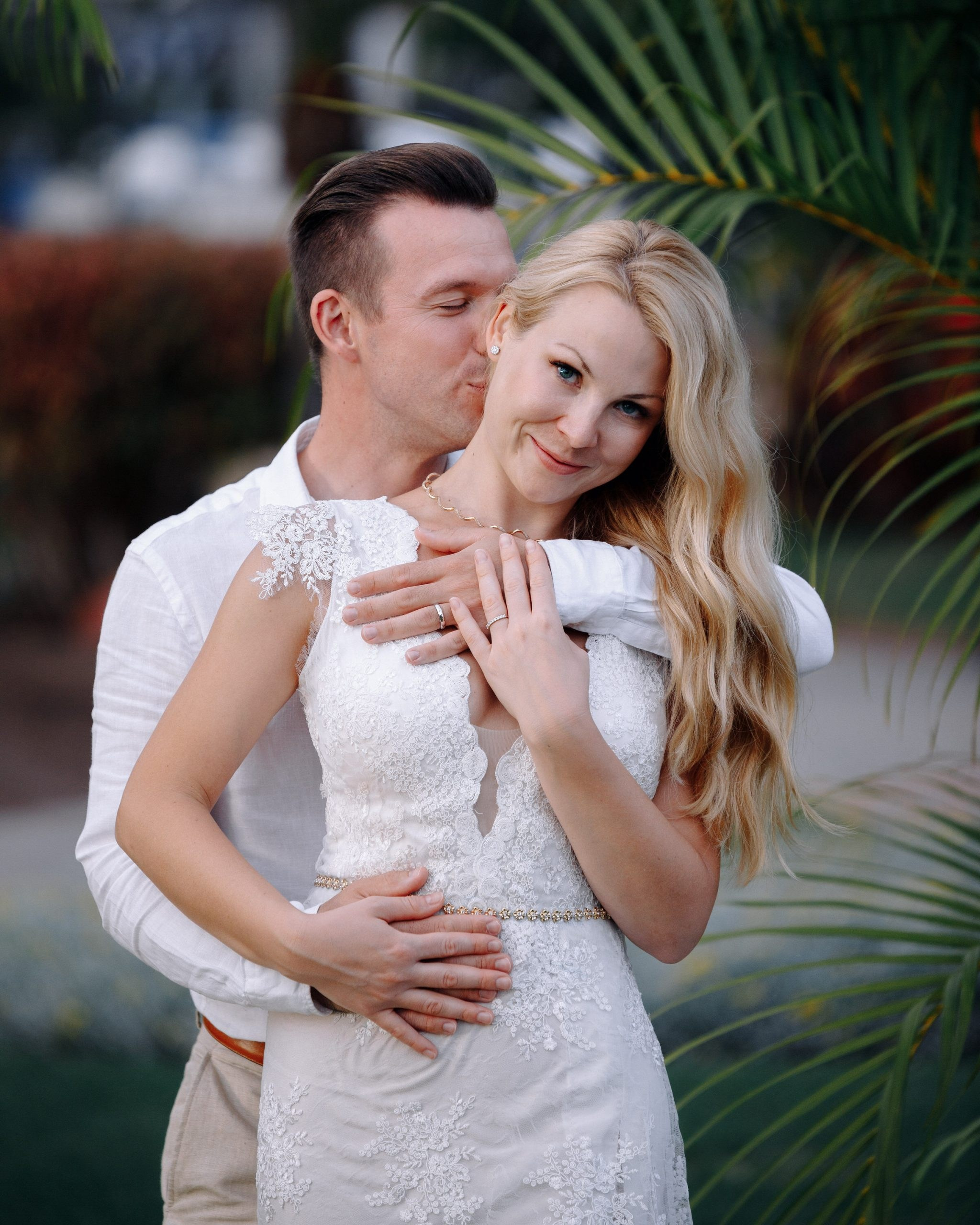 A bride and groom hugging in front of palm trees.