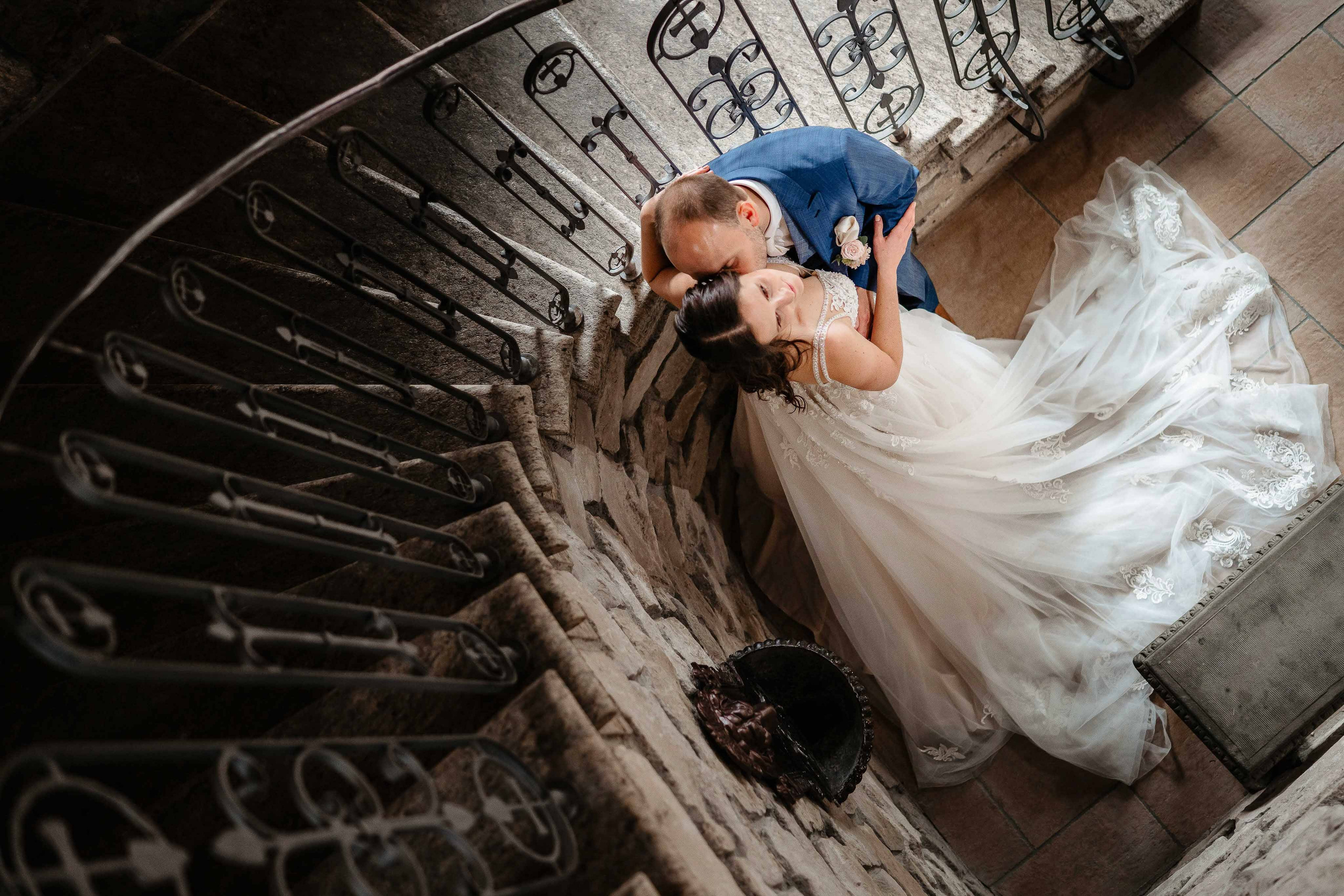 Brautpaar intimer Kuss auf historischer Wendeltreppe, emotionale Hochzeitsfotografie.