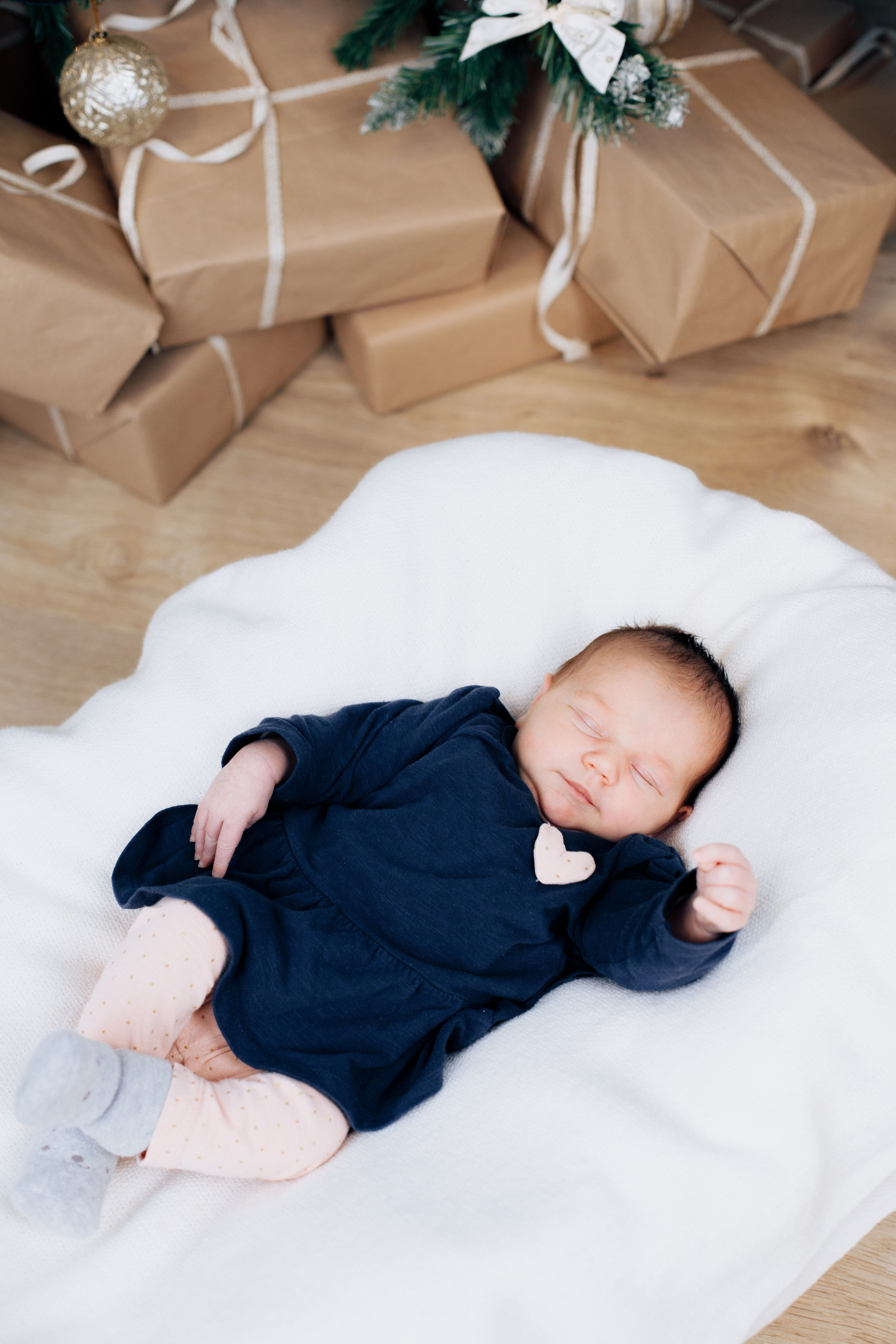 Baby liegt unter dem Weihnachtsbaum neben Geschenken. Ein festlicher und herzlicher Moment.