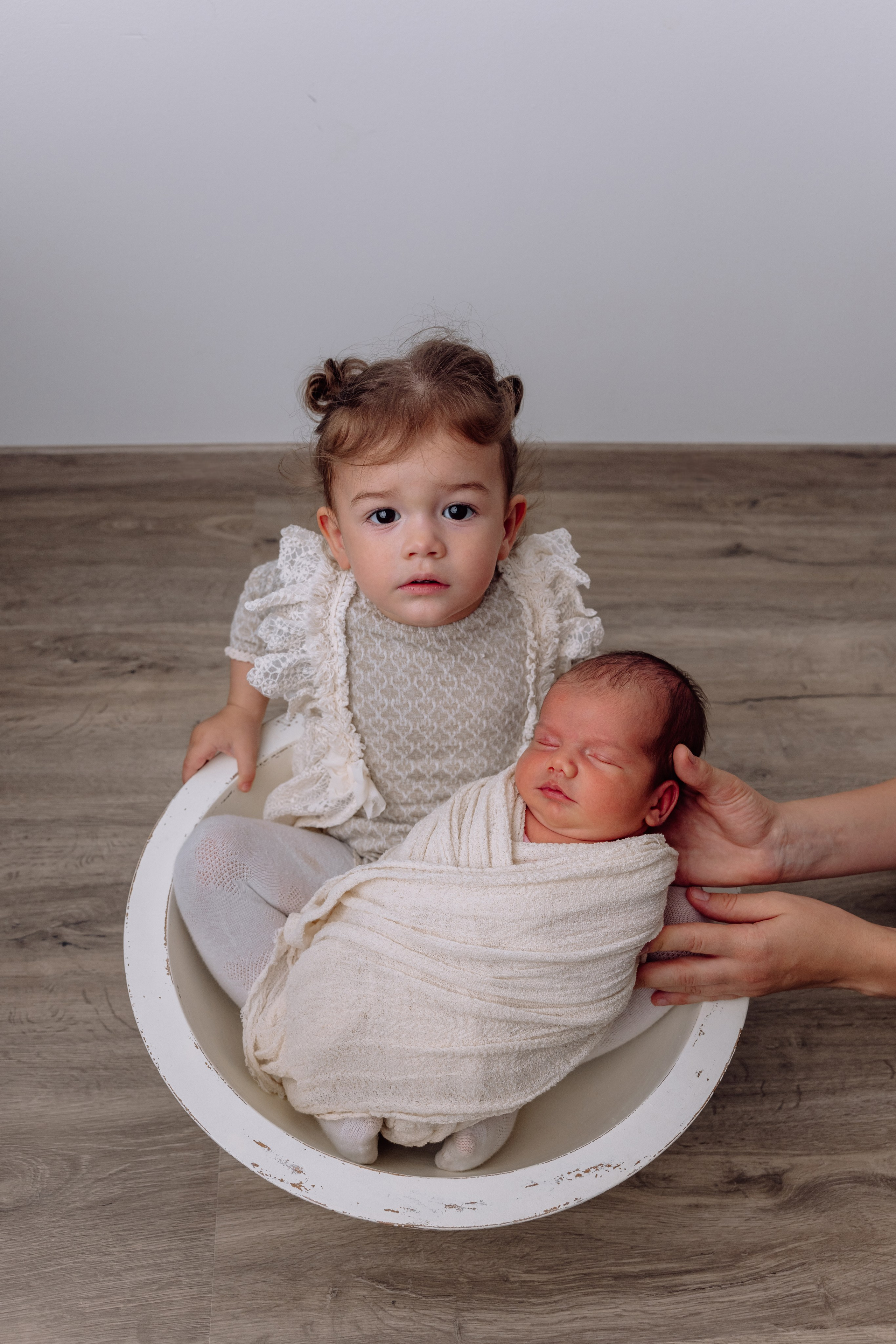 Zwei Geschwister zuhause – große Schwester schaut zärtlich auf das Neugeborene.