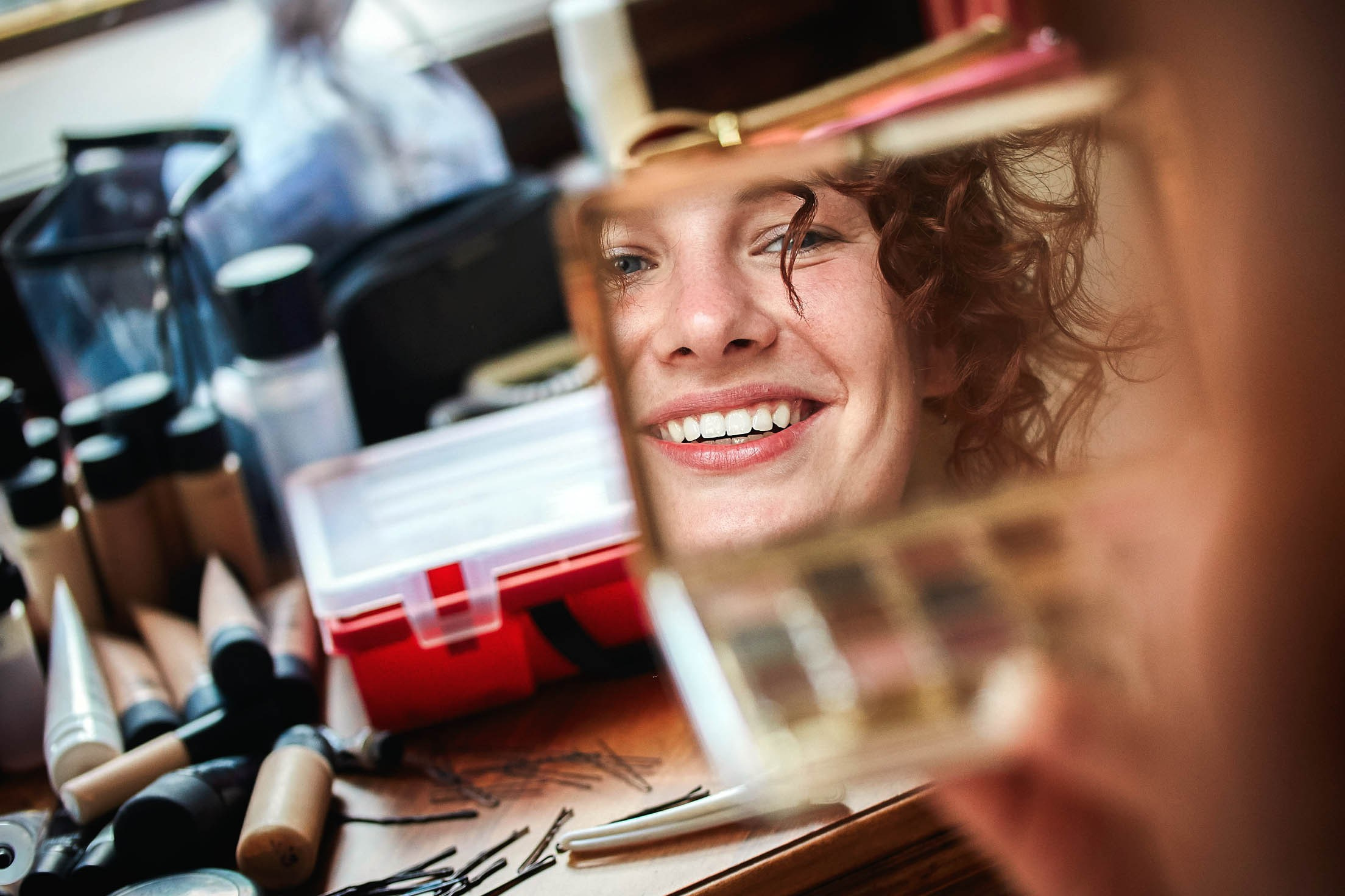 A happy, radiant red-haired bride smiles as she looks at her reflection during her bridal preparation in Cesky Krumlov.