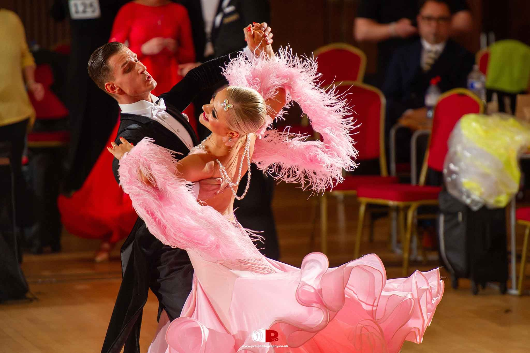 Ballroom dancers in pink feathered attire twirling gracefully in a dance competition.