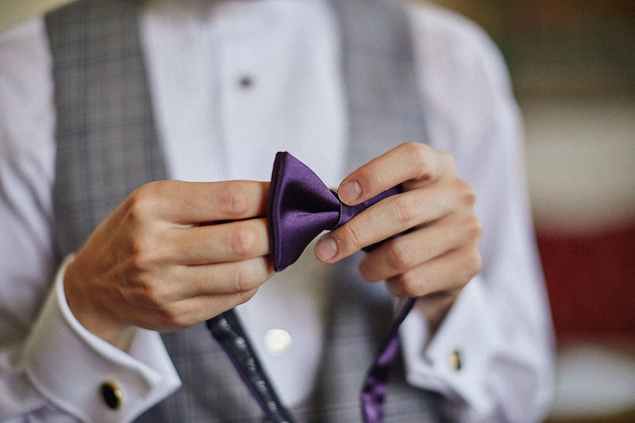 Close-up of groom's hands adjusting a vibrant purple bow tie at Vila Bled wedding.