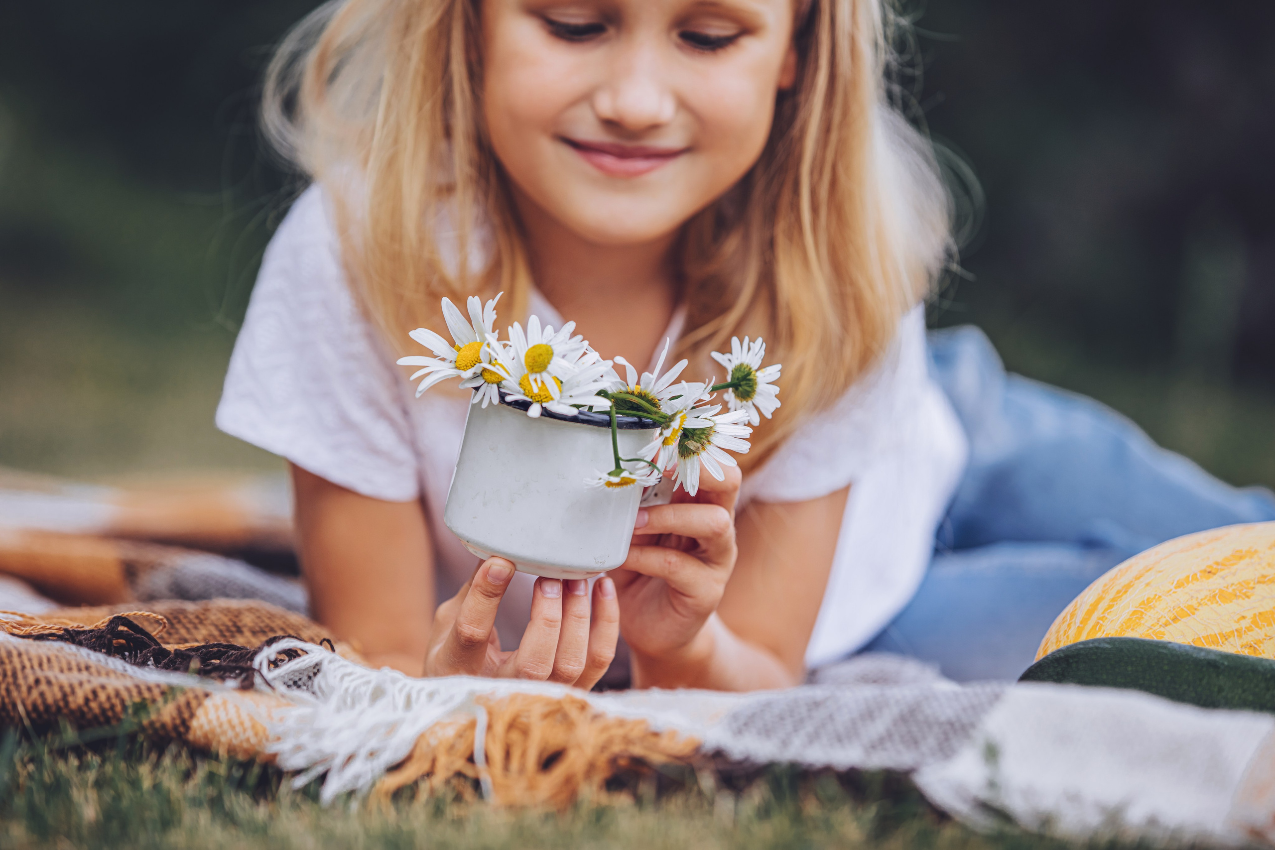 Petite fille blonde allongée sur un plaid, tenant des fleurs de marguerite avec tendresse