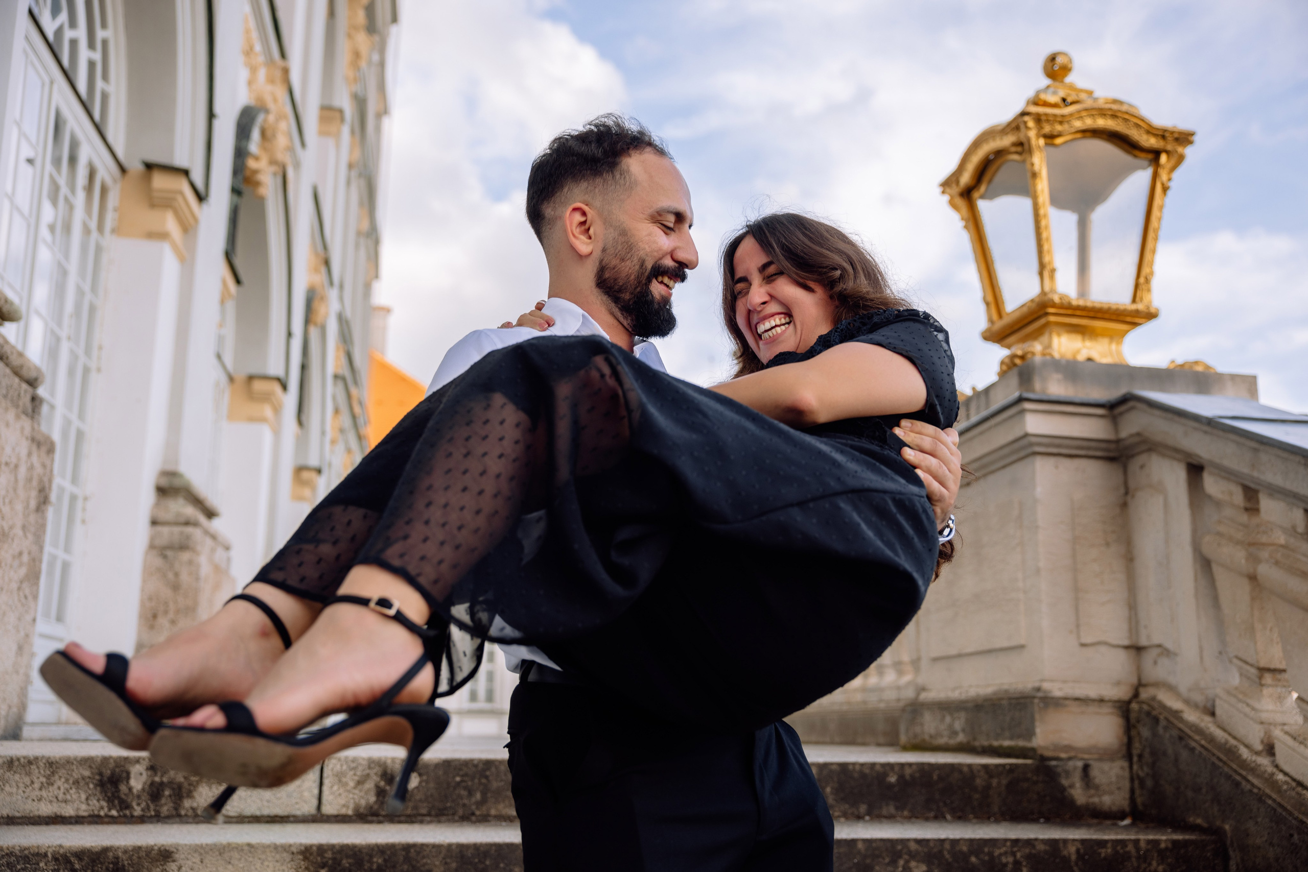 Bräutigam trägt die Braut auf den Armen die Treppe hinauf vor dem Schloss Nymphenburg