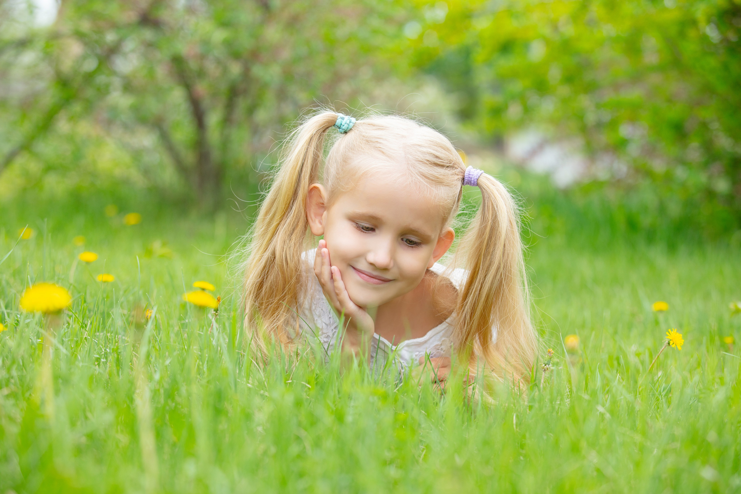 Petite fille allongée dans l'herbe verte avec des couettes, sourire naturel