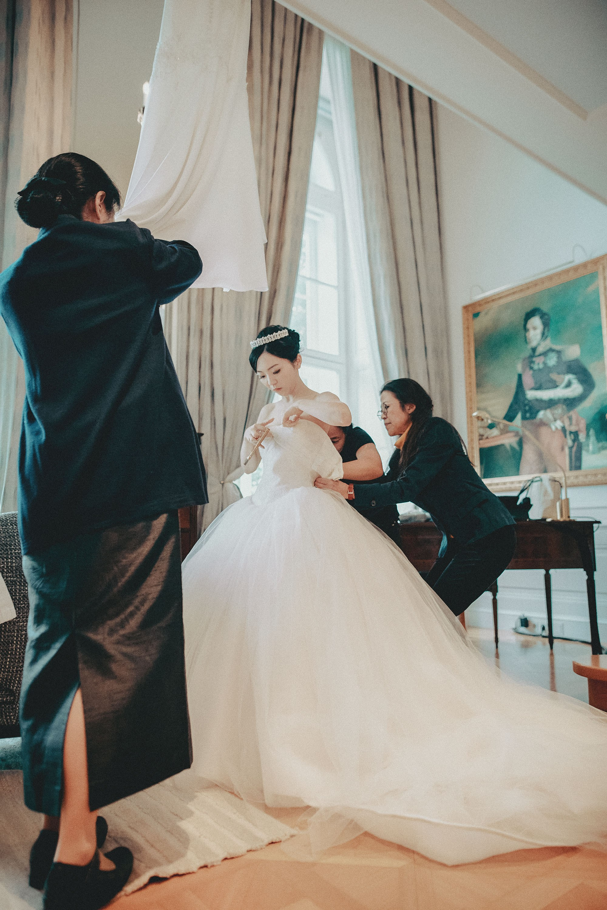 The bride is assisted by the makeup artist and staff into her wedding dress.
