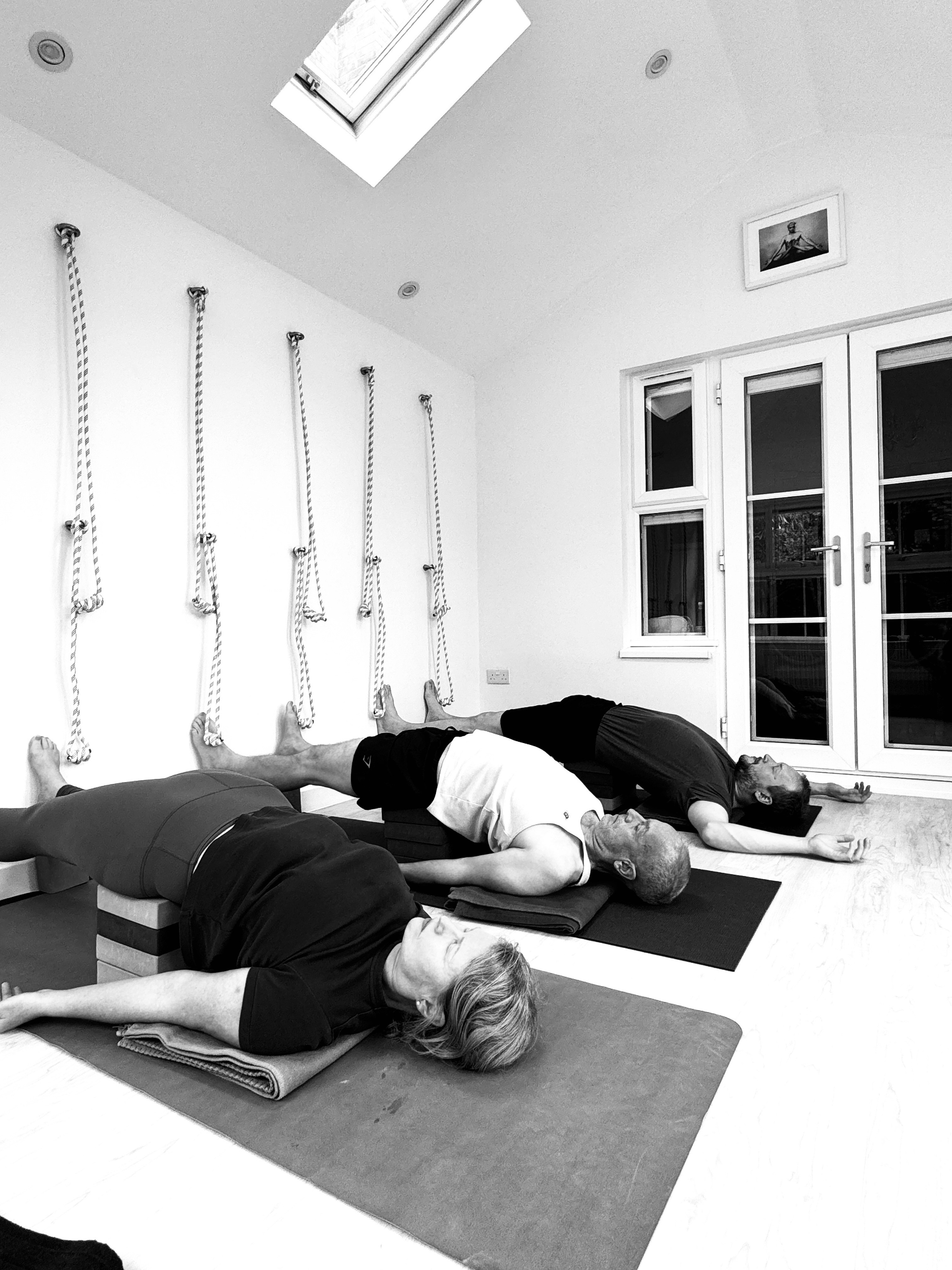 Calm and intimate Iyengar yoga session in Solihull, mats neatly arranged, teacher assisting students.