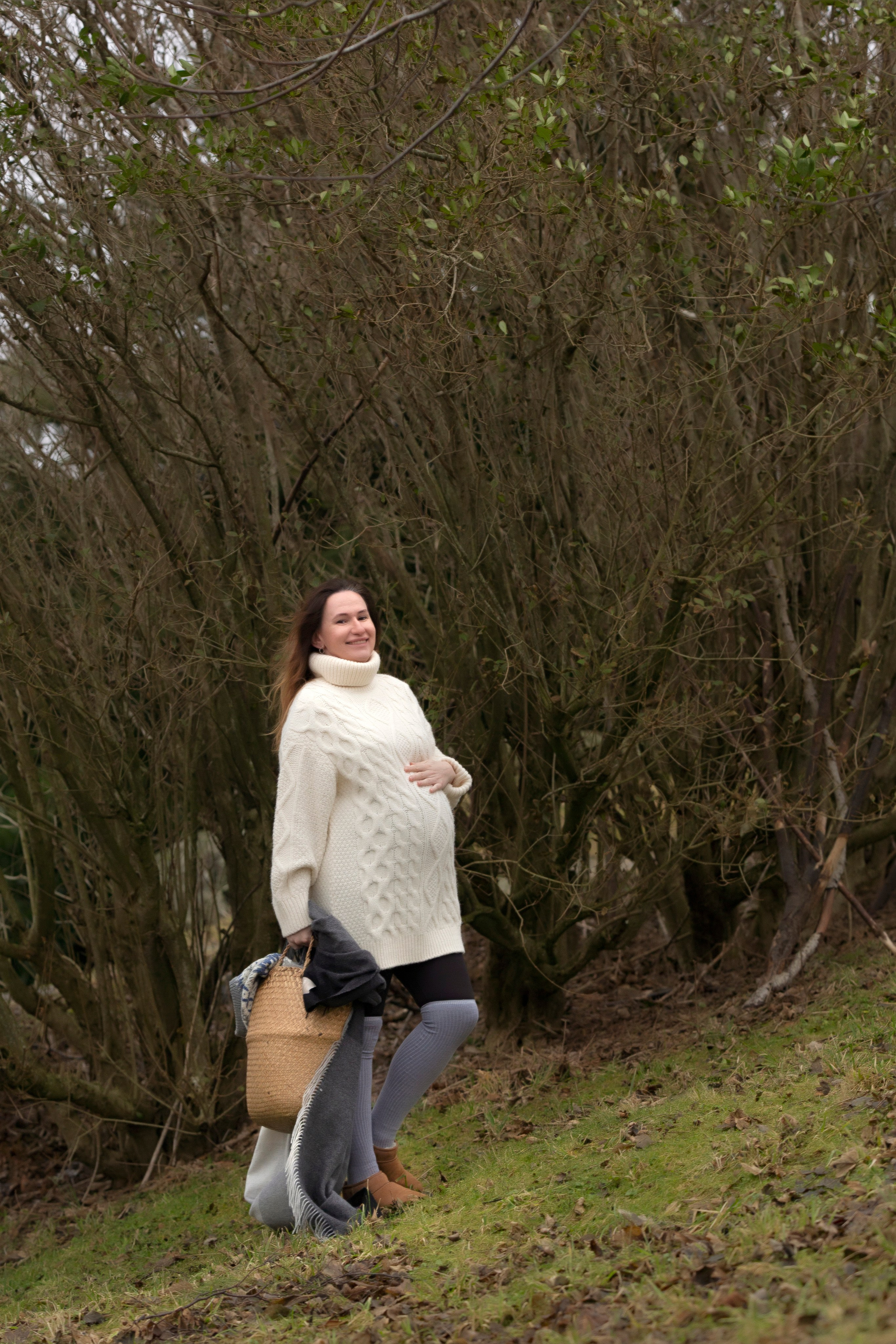 Pregnant woman standing gracefully by a tree, captured in a tender nude style, celebrating the beauty of maternity