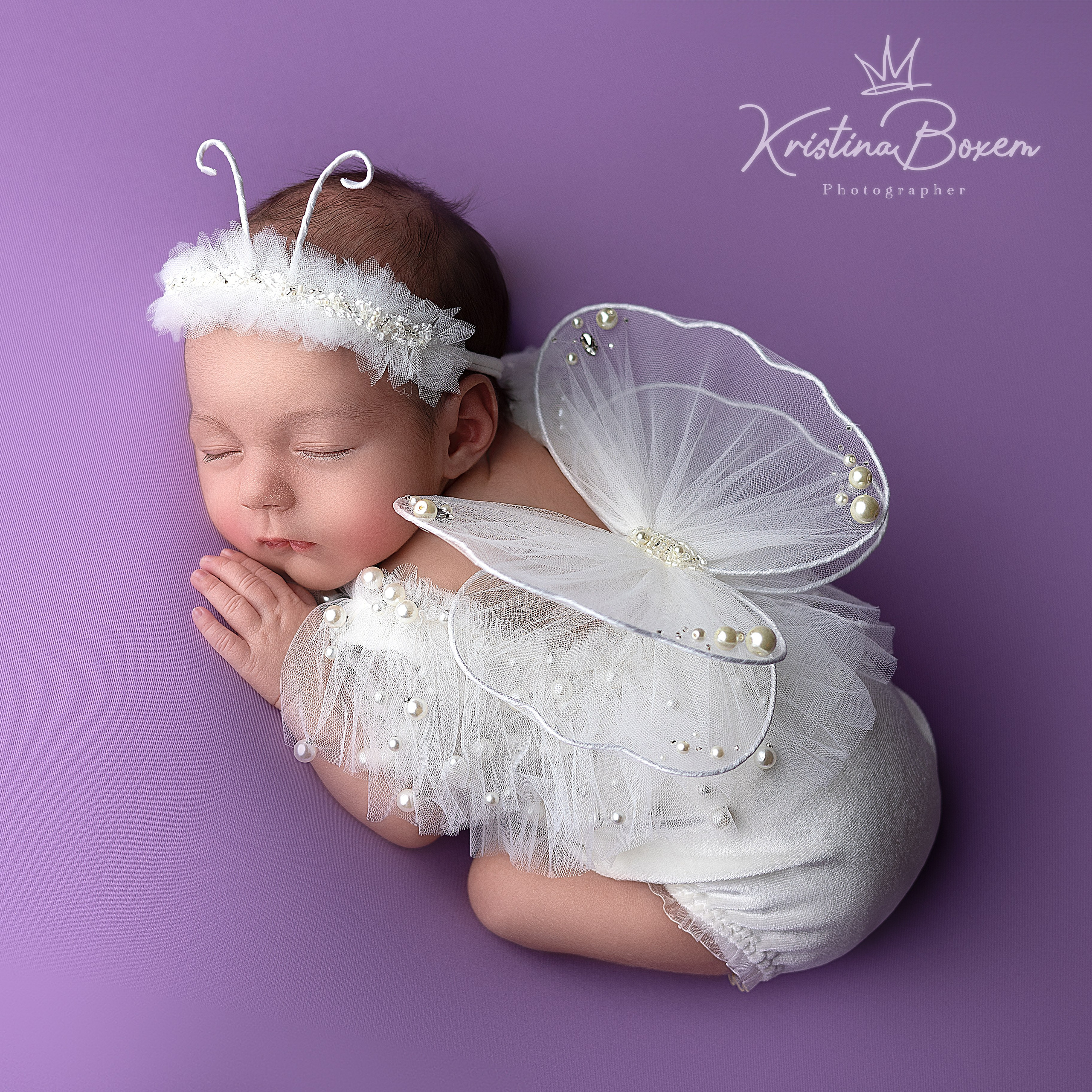 Pasgeboren baby in de gedaante van een delicate witte vlinder, slapend op een paarse achtergrond – een sprookjesachtige newborn fotoshoot door Kristina Boxem.
