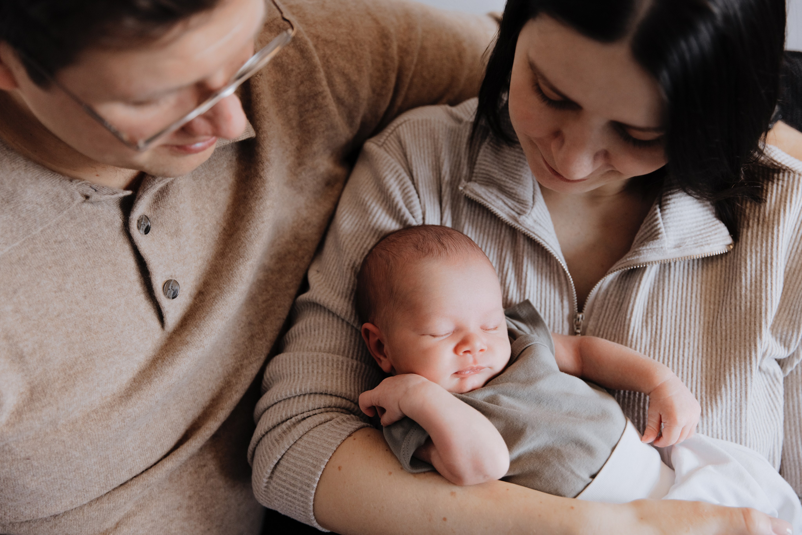 Neugeborenes liegt liebevoll in den Armen der Mutter, während der Vater die beiden umarmt.