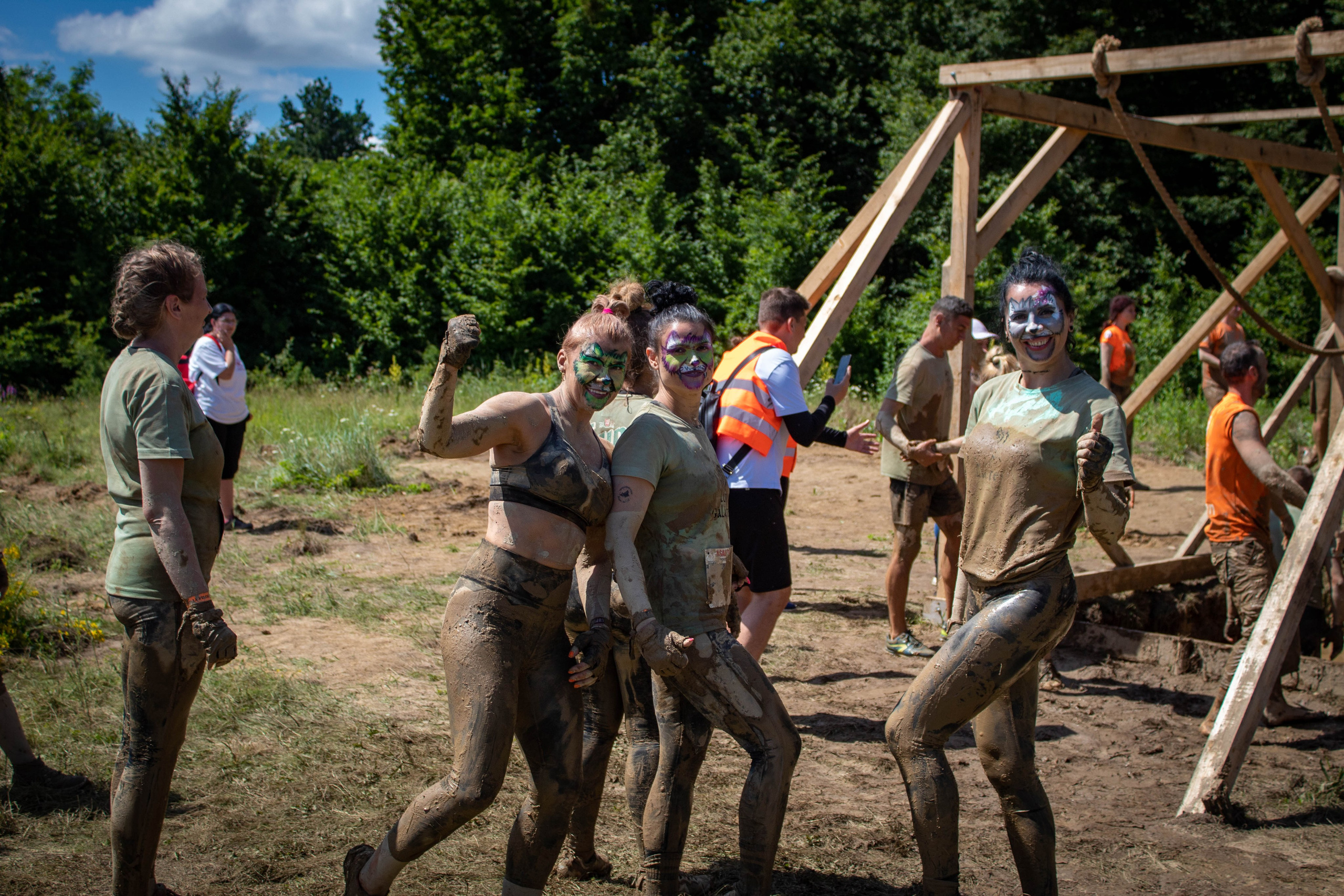 Competitors helping each other climb a wooden obstacle in an outdoor challenge course.