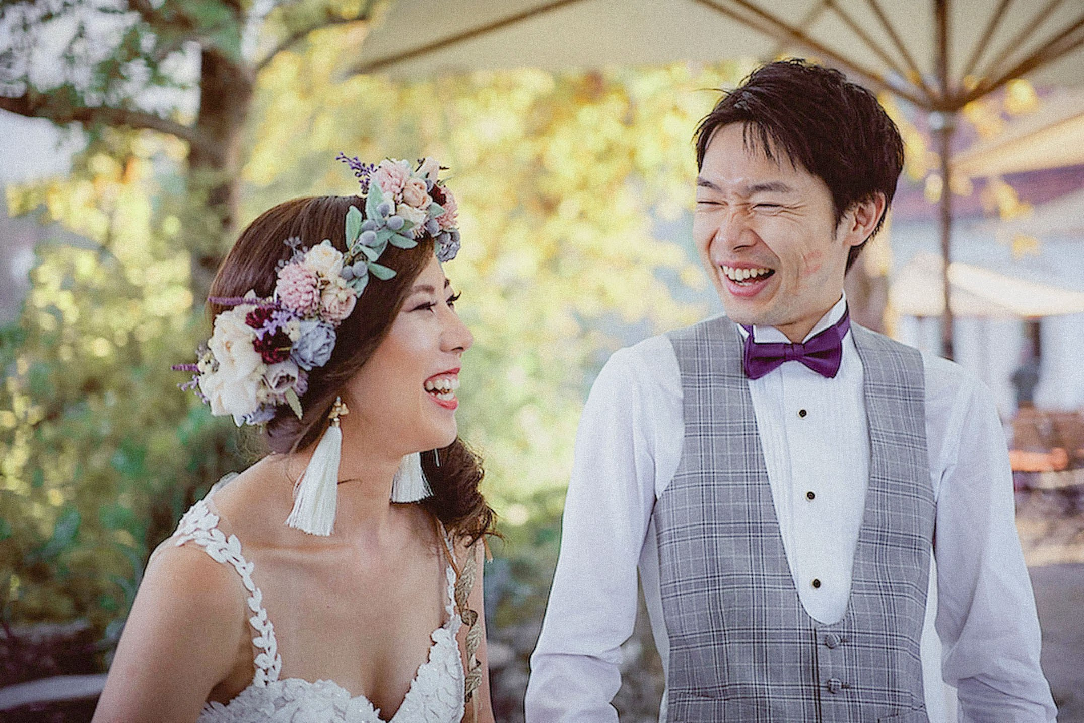 A Japanese bride, wearing a floral headpiece, and her groom laugh out loud during their wedding day.