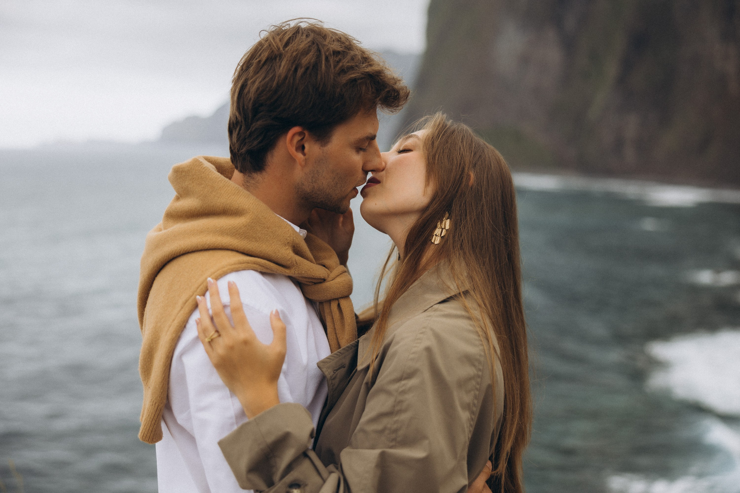 Beautiful engagement moment by the ocean in Madeira, Portugal, as one partner kneels to propose while waves crash in the background.