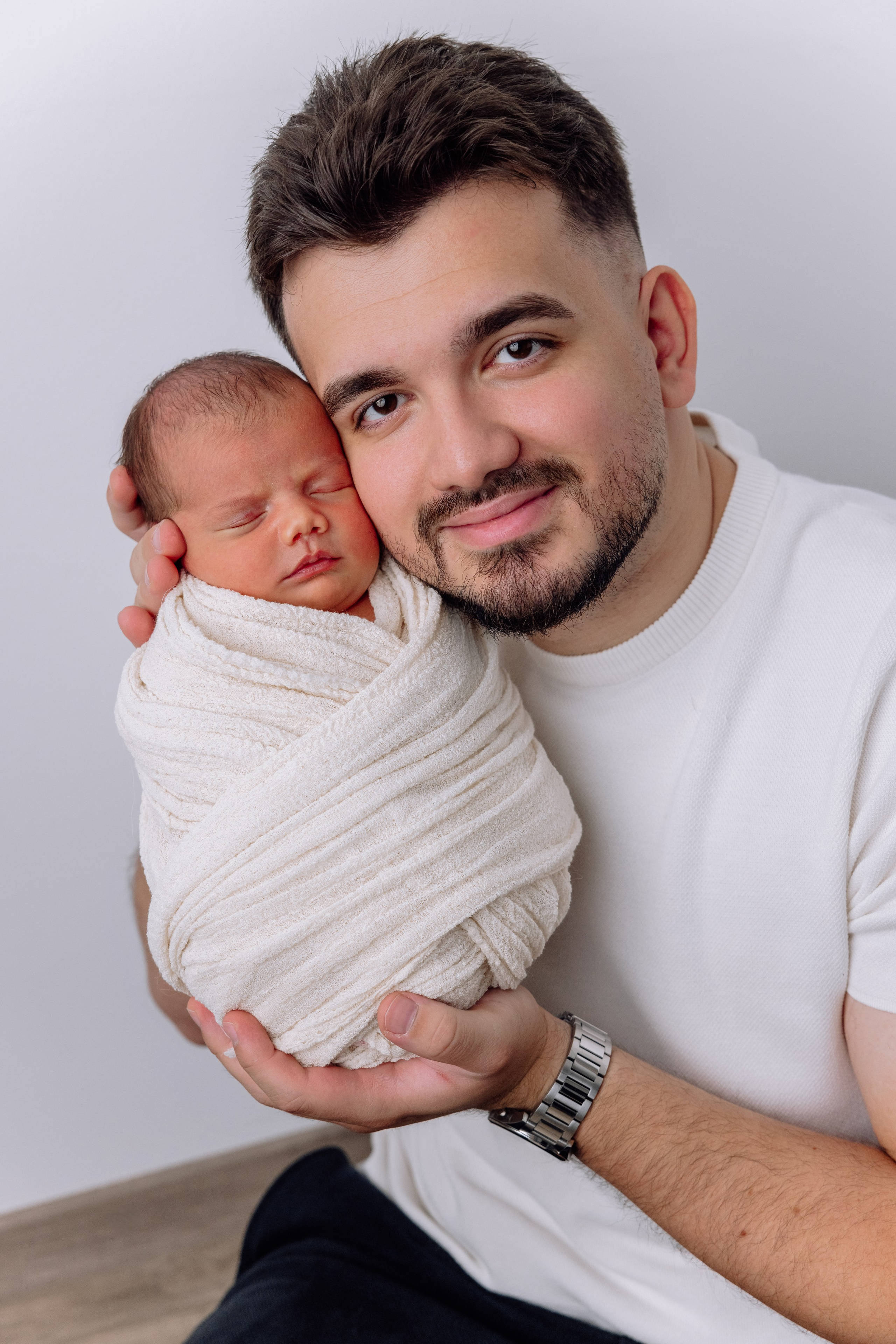 Familienmoment zuhause – Vater hält das eingewickelte Baby liebevoll an seiner Wange.