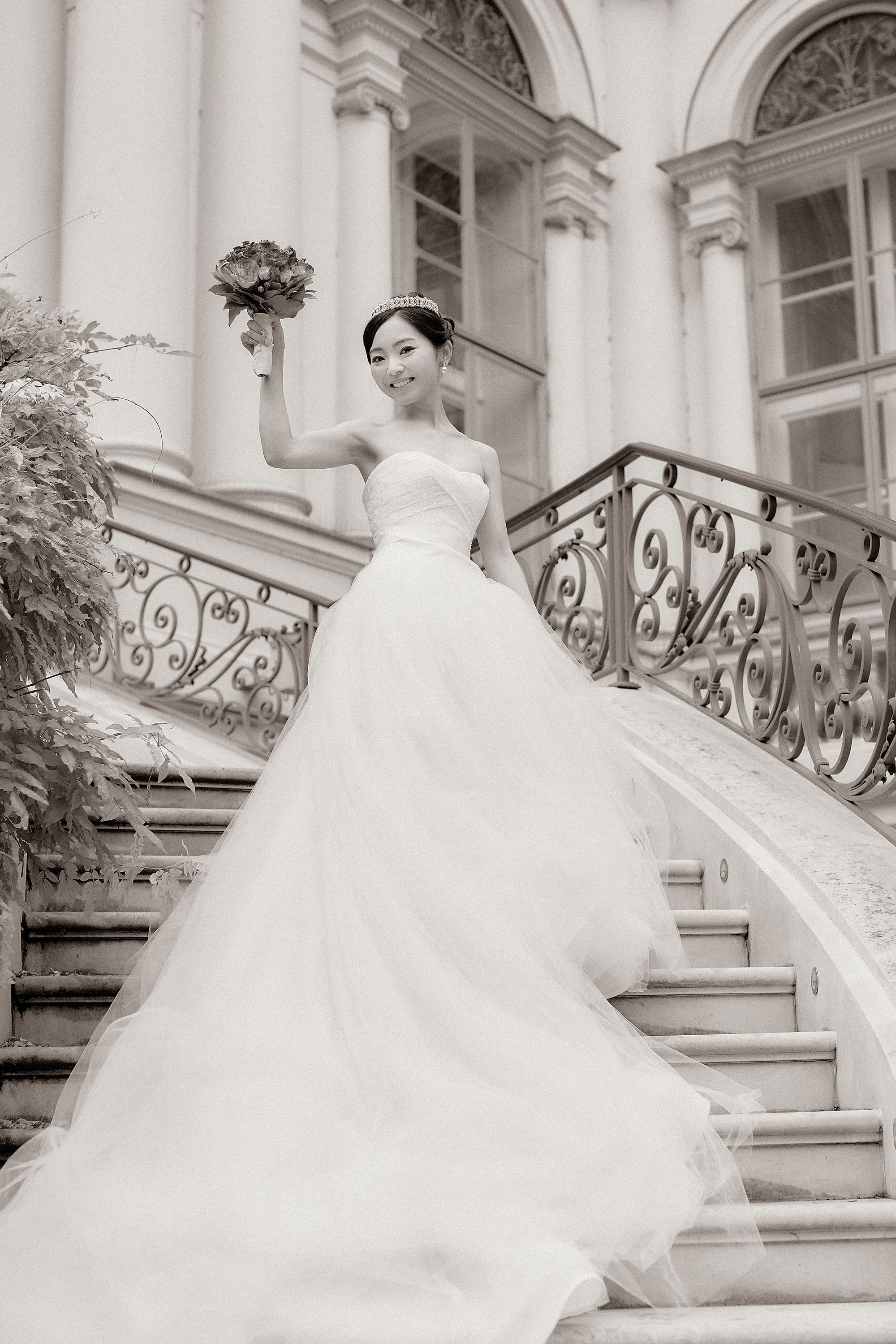 The bride raises her bouquet as she stands atop the historical steps of the Palis Coburg.