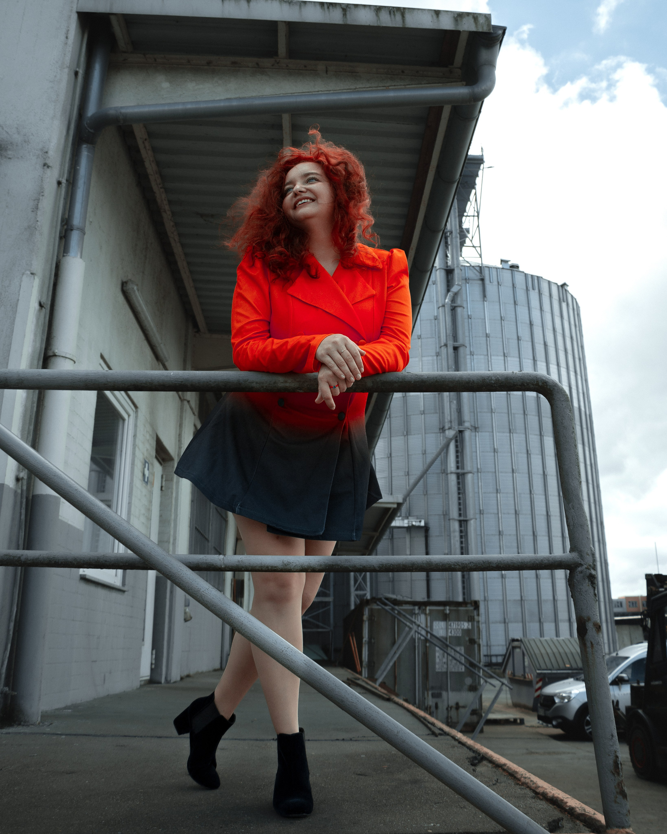 Ksenia posiert vor Fabrik – auffällige rote Haare und intensives rotes Kleid