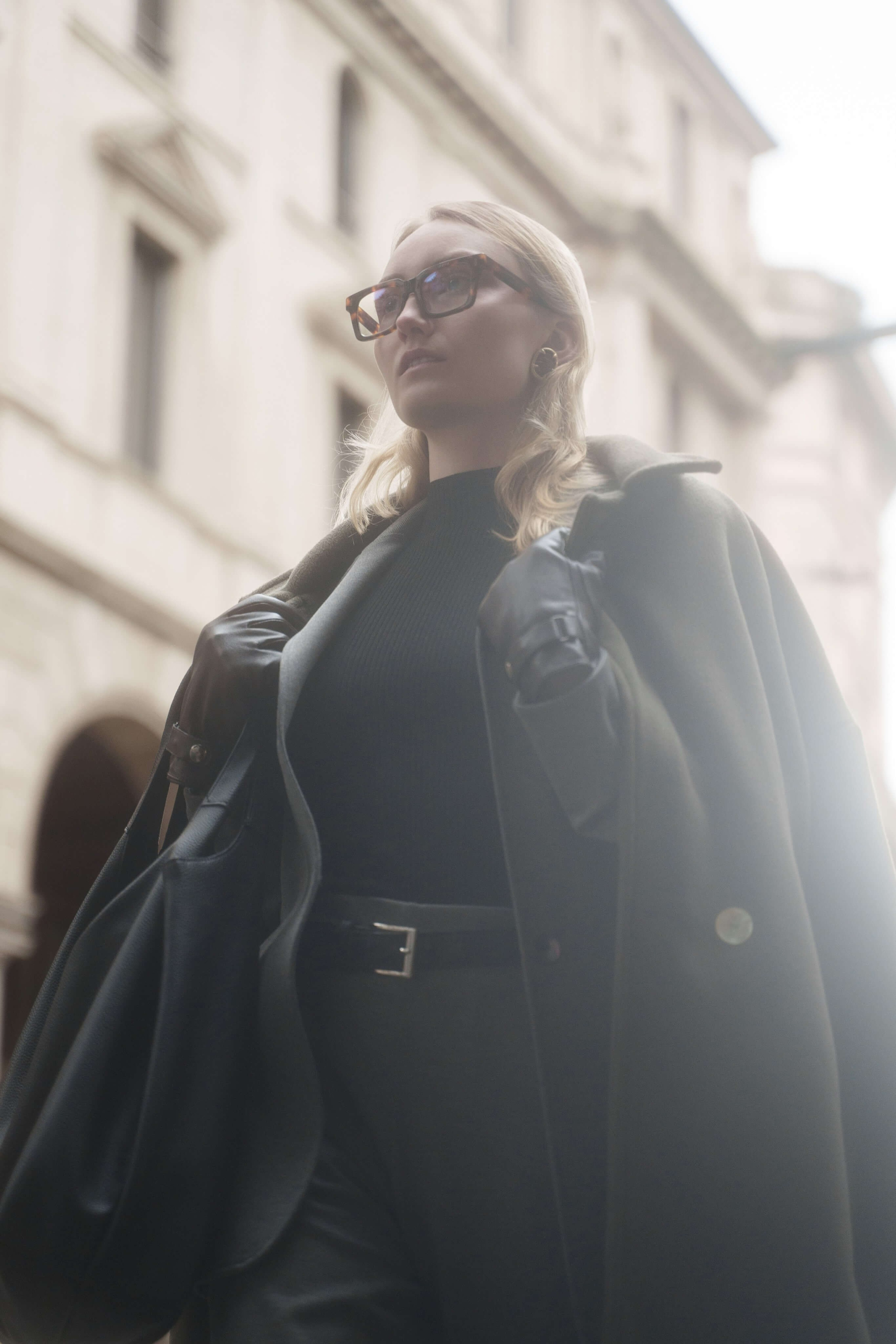 Backlit portrait of a blonde woman in oversized coat and square eyeglasses in Milan