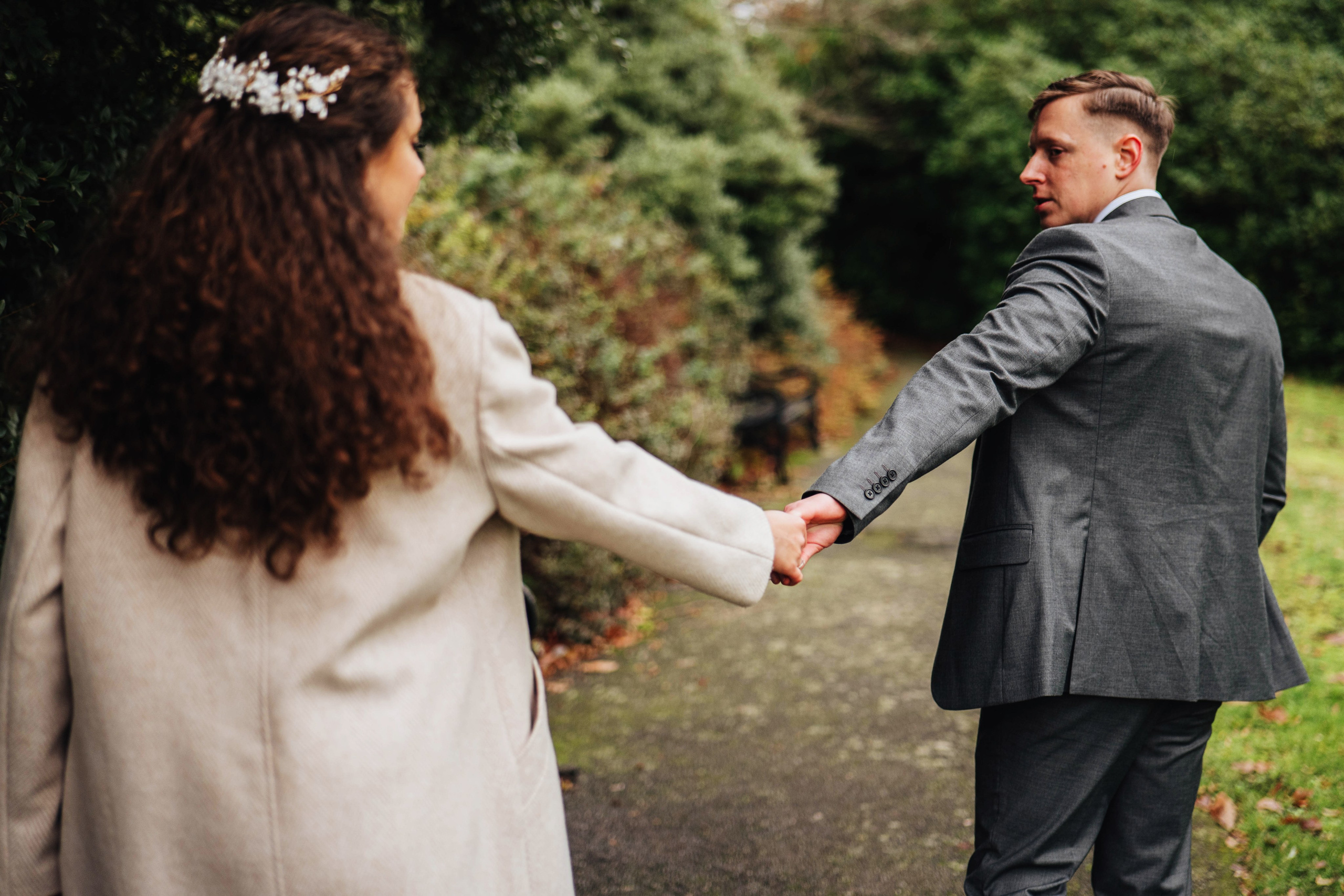 bride and groom holding hands while walking in the park